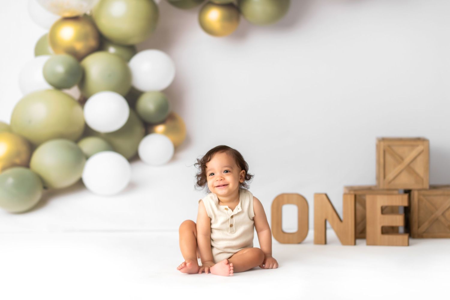 Simple white studio setup with sage green balloons and wooden blocks.