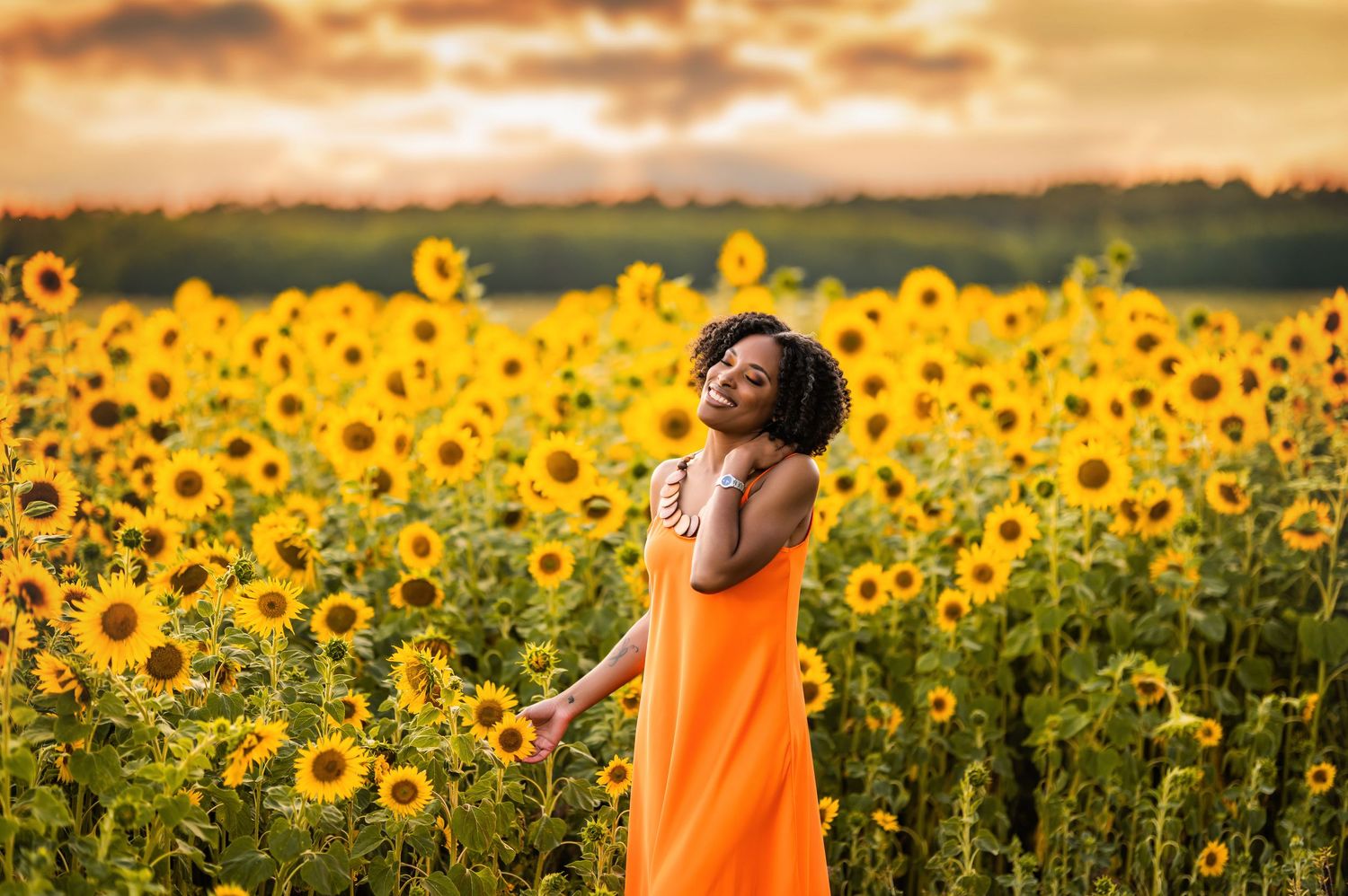 Woman in orange dress standing in sunflower field at sunset, arms outstretched, enjoying nature.