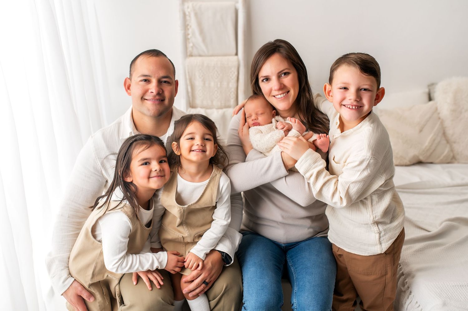 Joyful family portrait on white bed in neutral colored clothing.