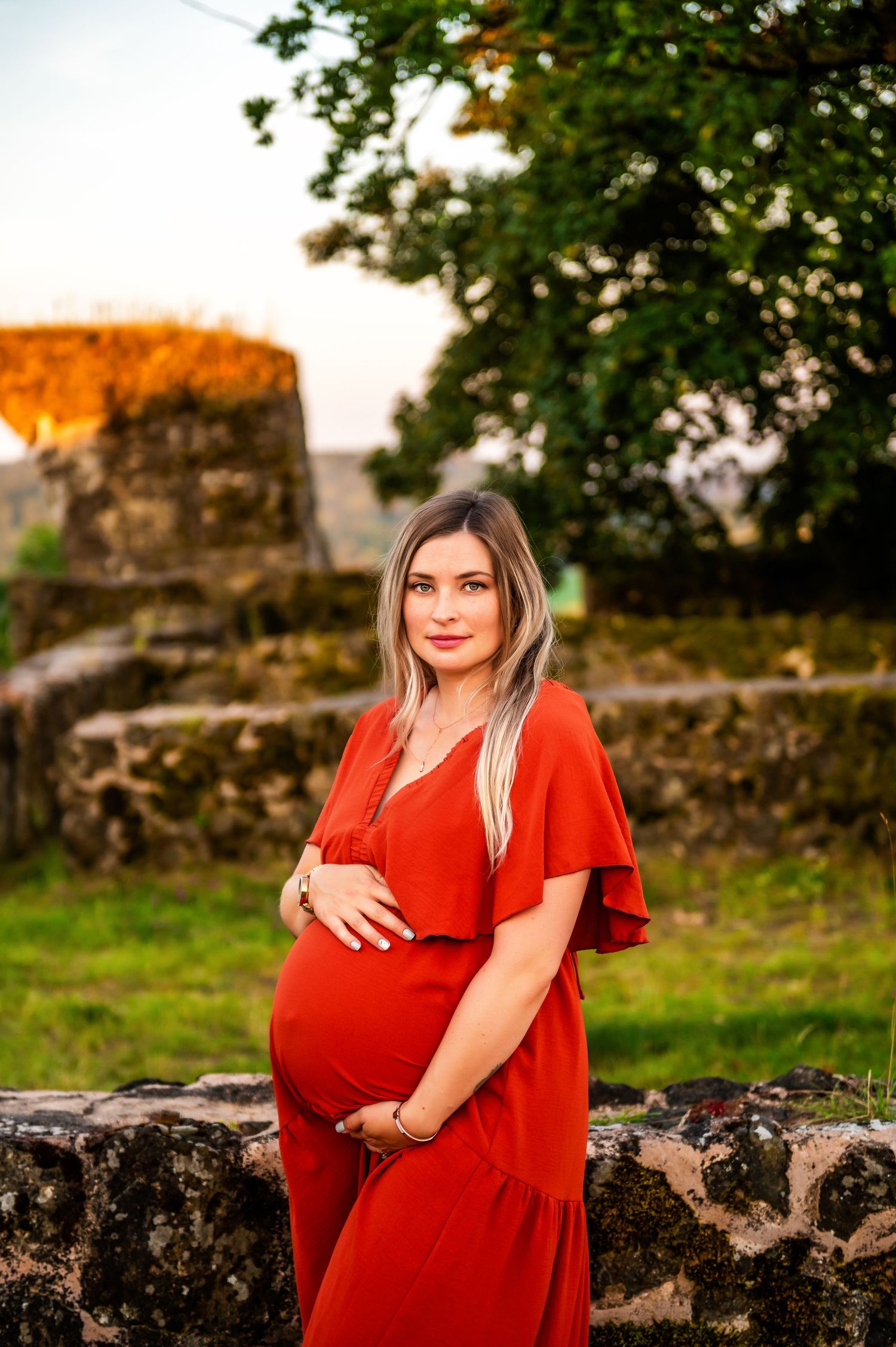 A maternity portrait in a vibrant red dress against ancient stone ruins at sunset.