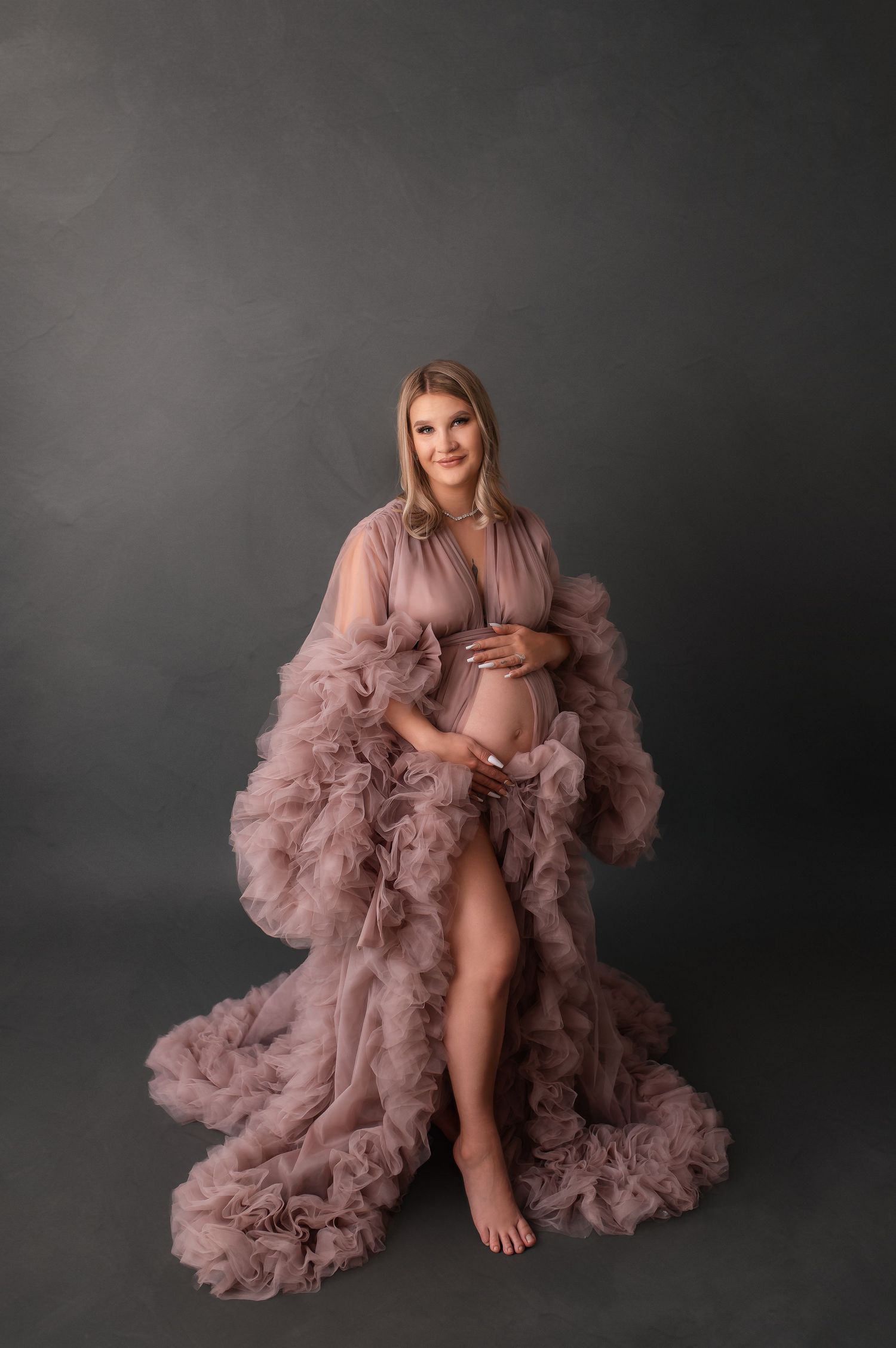 Artistic maternity photo featuring dramatic mauve tulle robe against dark background.