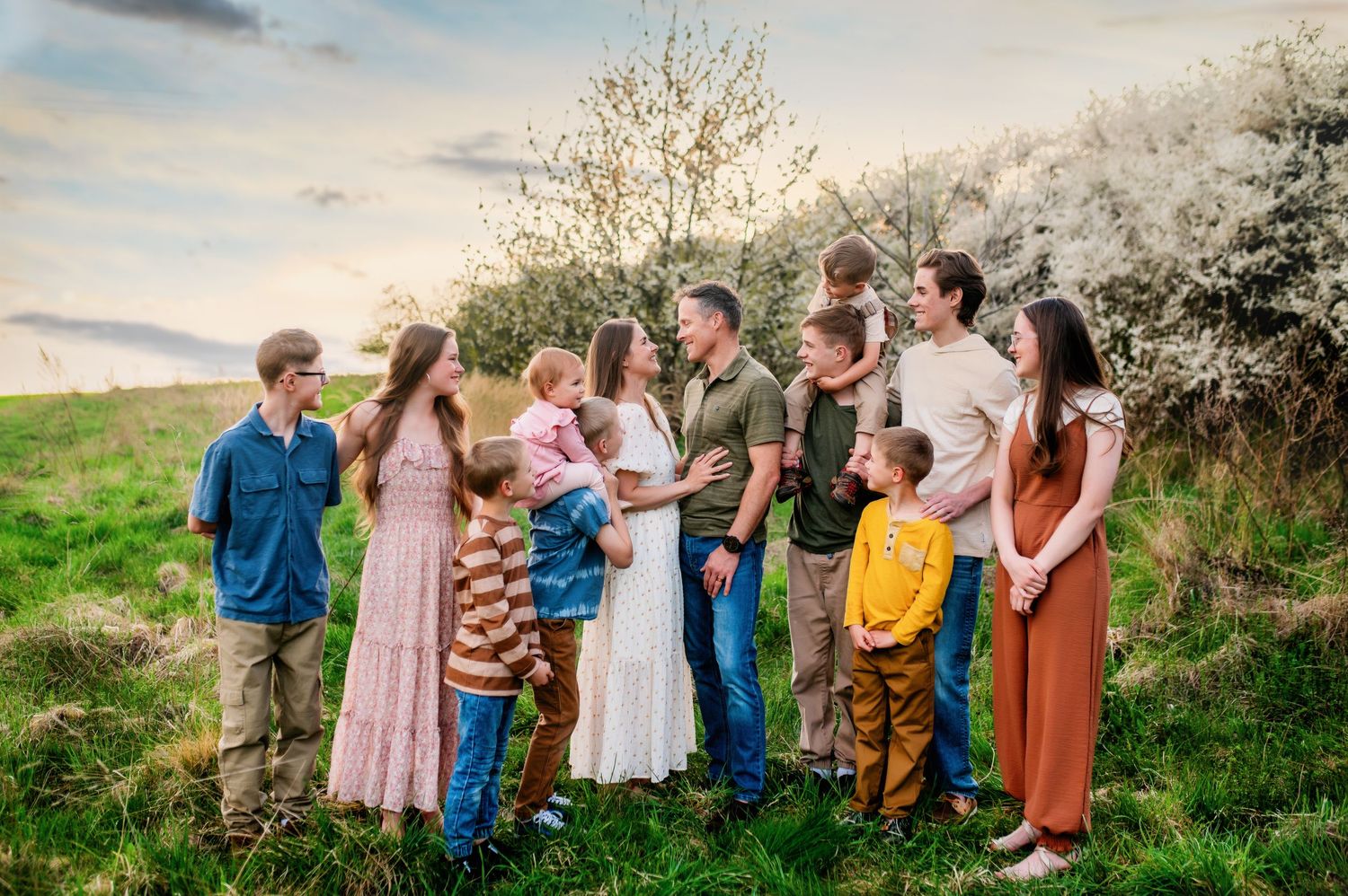 Group portrait of extended family members posed together in casual attire against spring blossoms at sunset.
