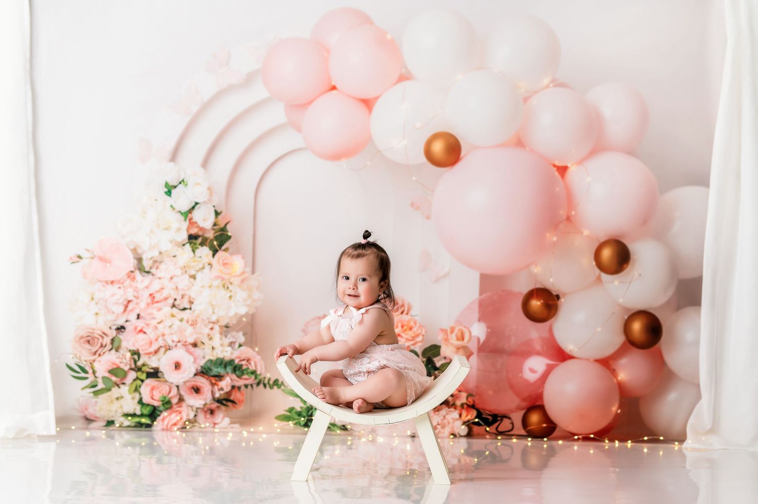 Elegant pink and white balloon arch setup with floral accents for special occasion photography.
