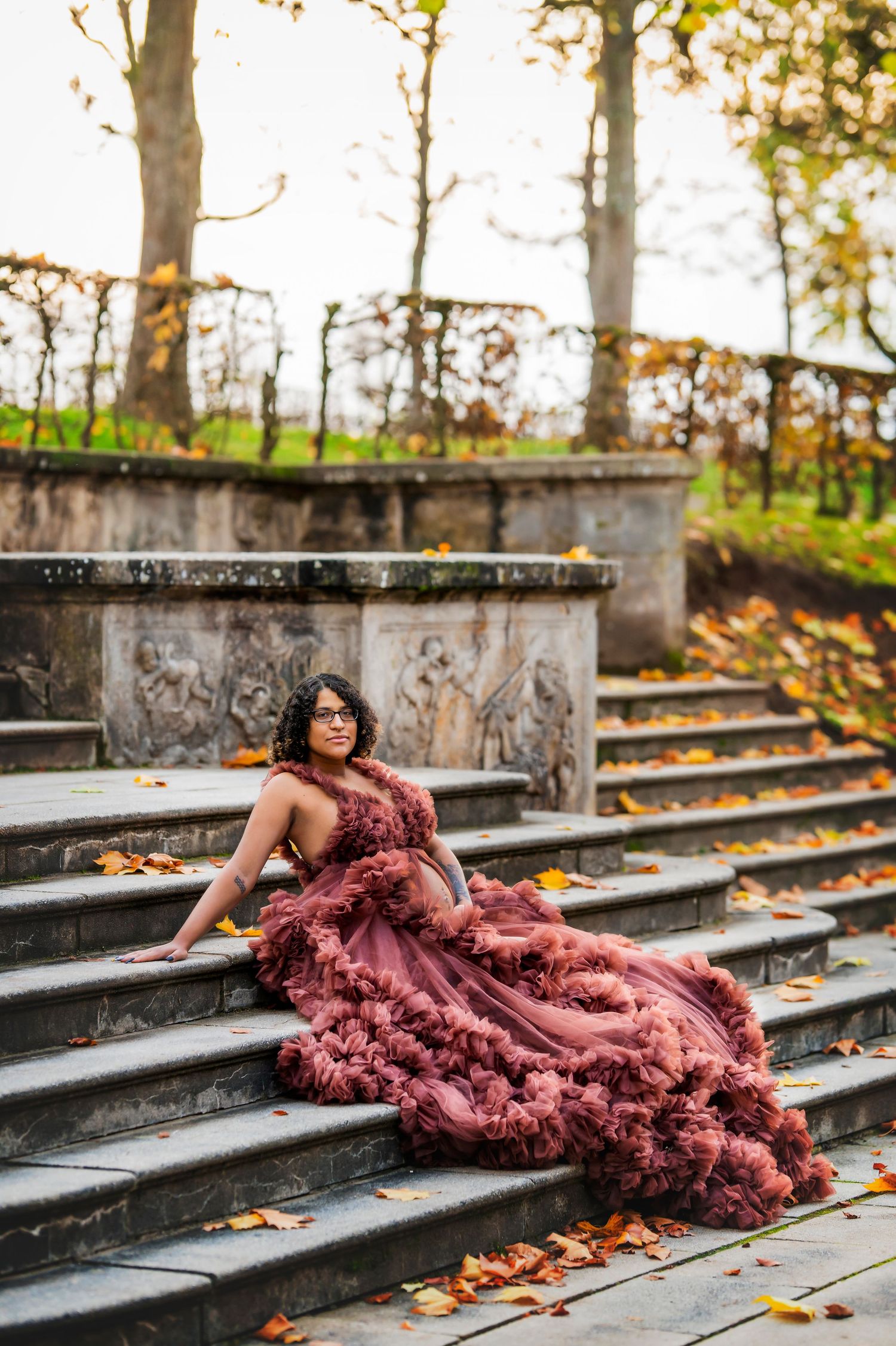 Dramatic maternity portrait on stone steps with flowing burgundy gown and fallen autumn leaves.