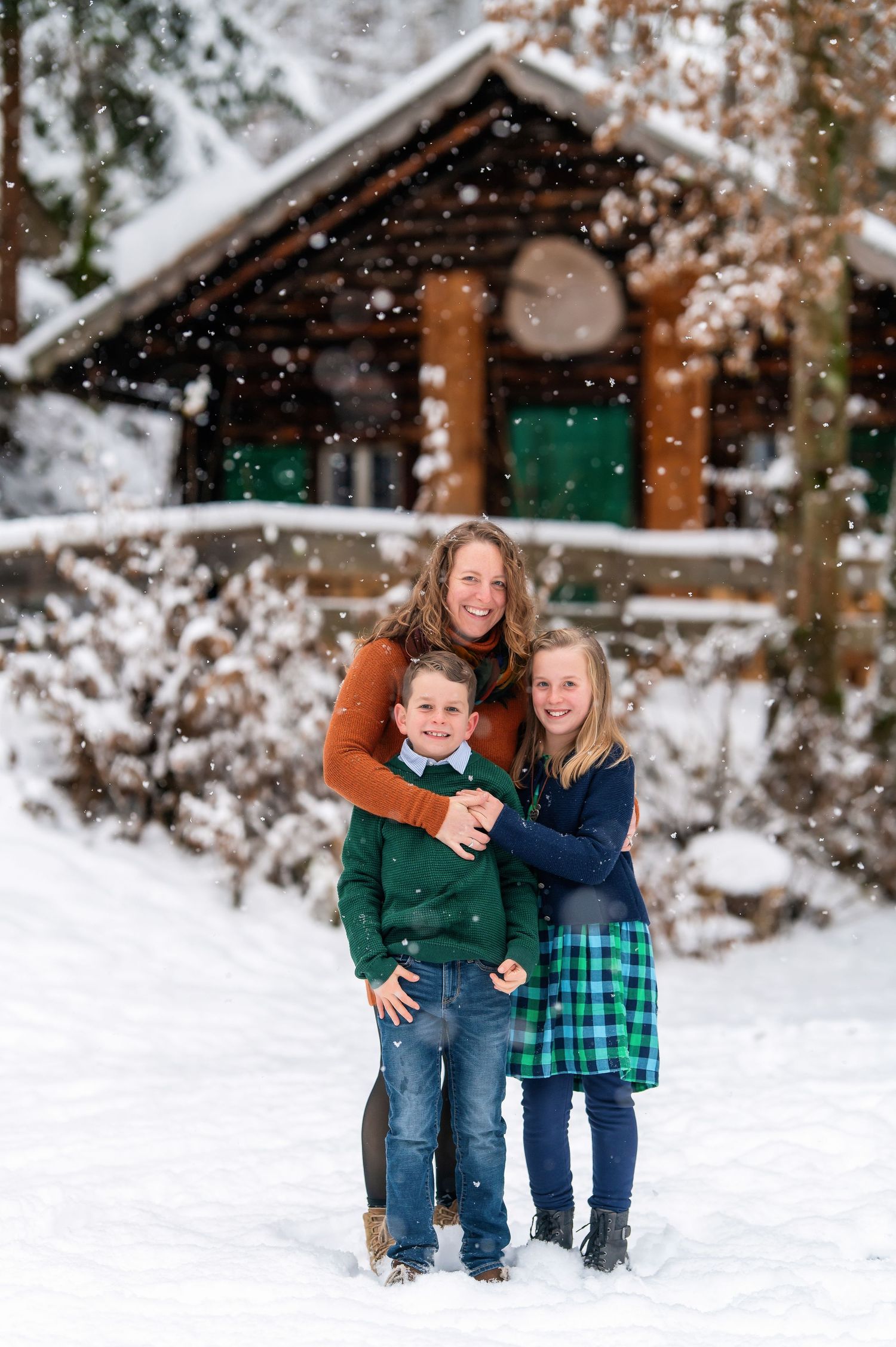 Three people pose playfully together in the snow with a wooden cabin in the background.