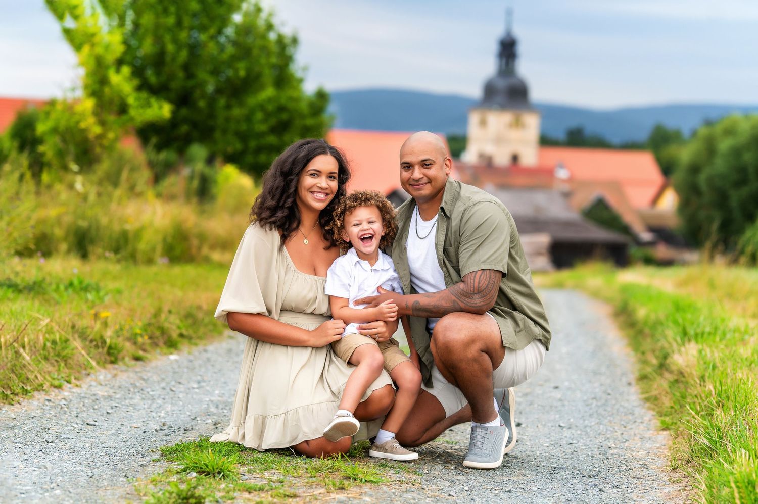 A family sits and plays together on a gravel path during an outdoor photoshoot session.
