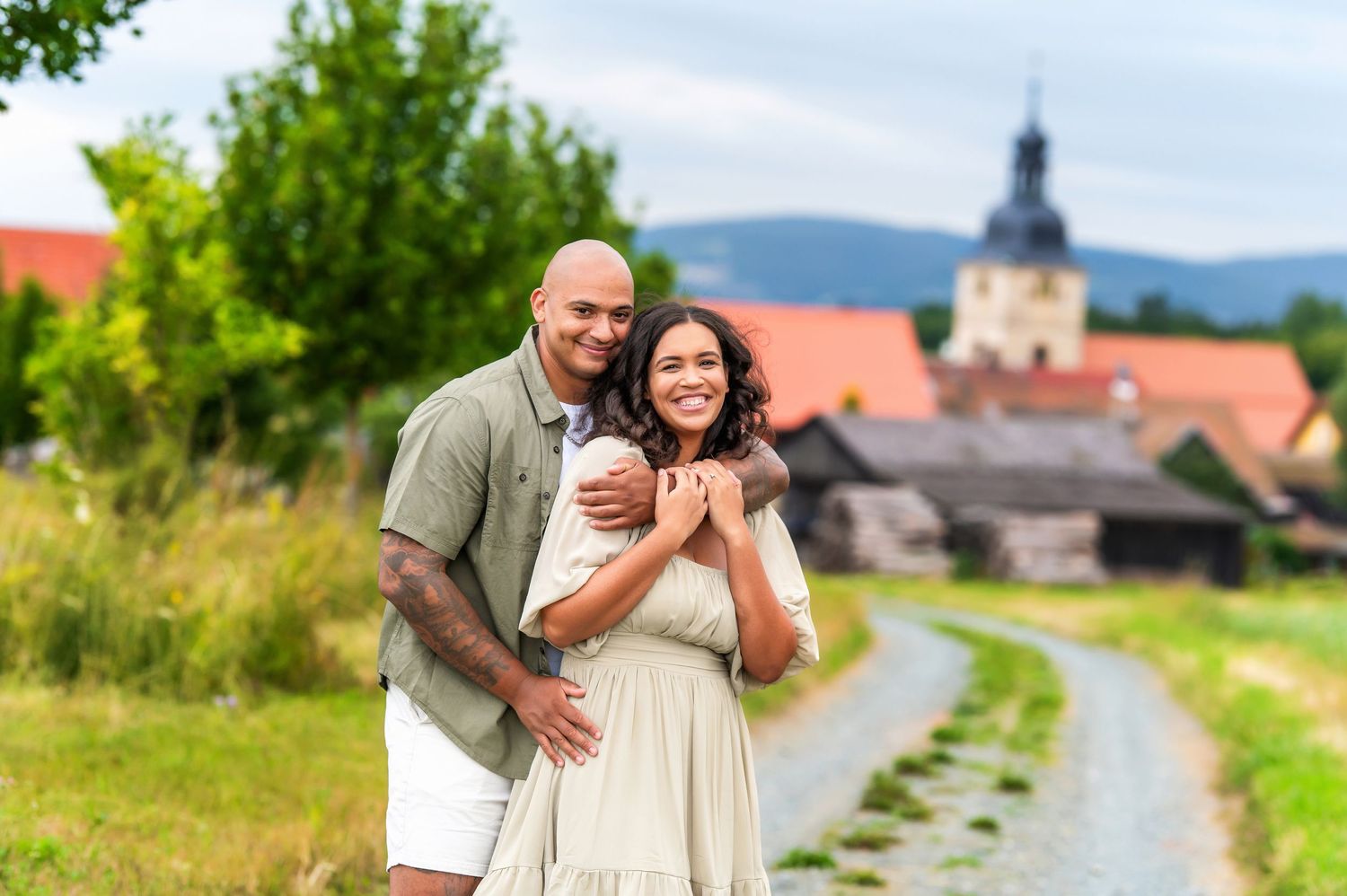 Loving couple embracing on a scenic countryside path with village church in distance.