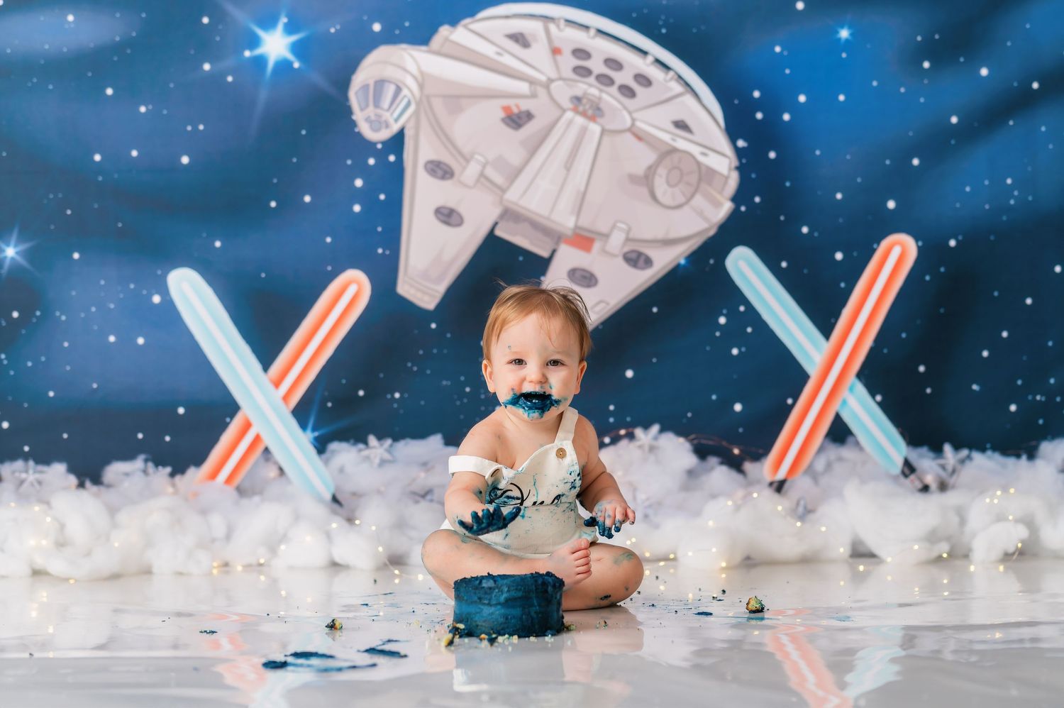 Star Wars themed baby photo with Millennium Falcon prop and lightsabers in a starry galaxy setting.