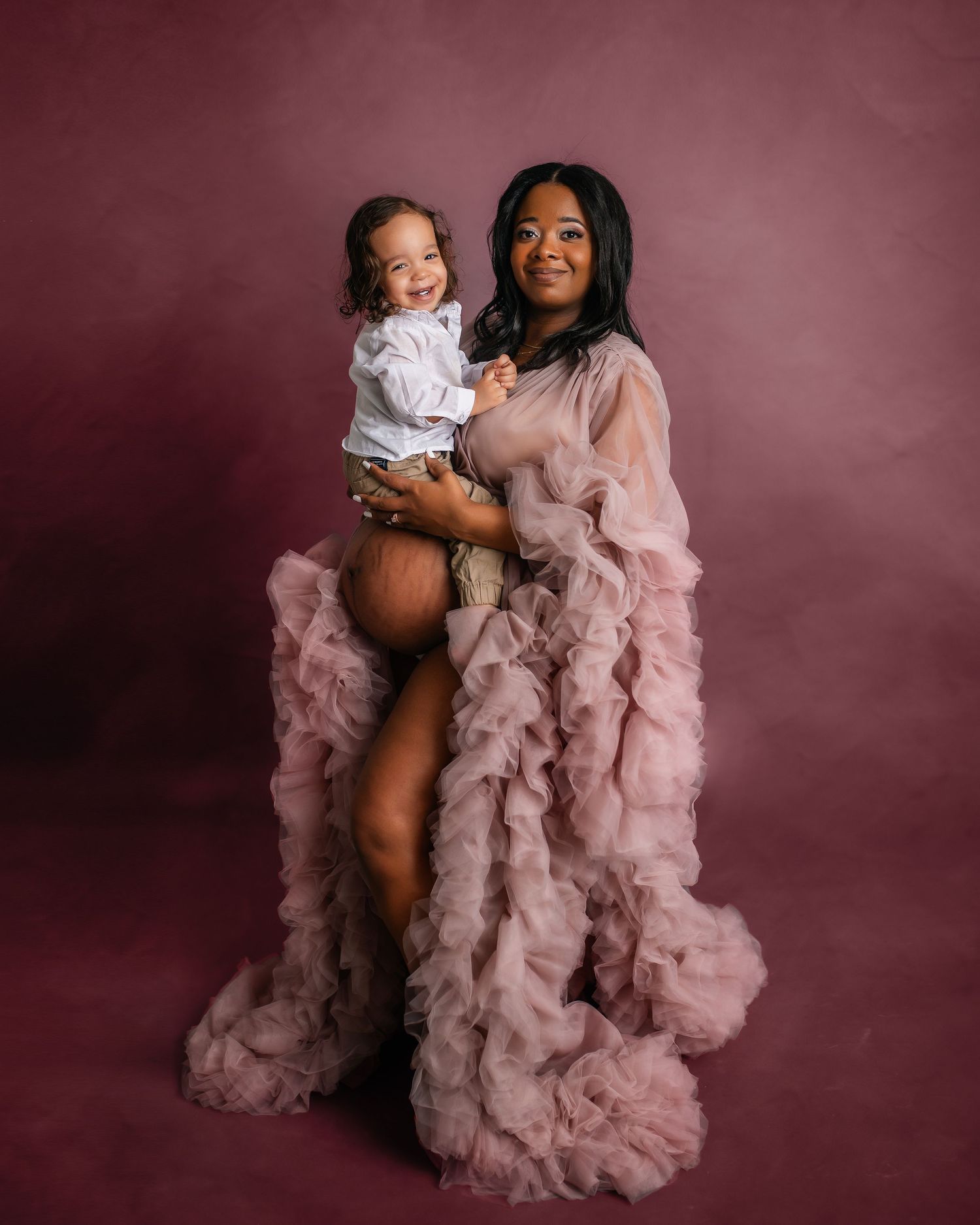 Mother and child portrait with pink ruffled dress against burgundy background.