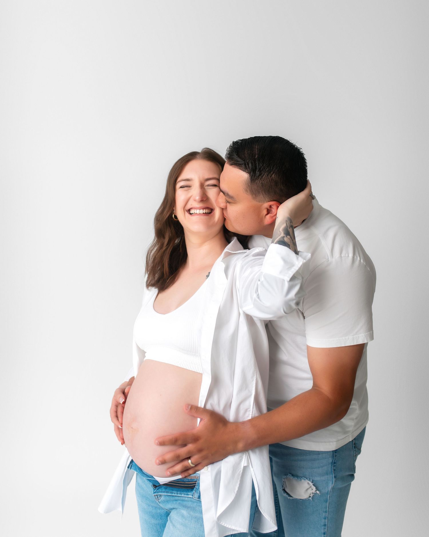 Intimate maternity photo of couple sharing tender moment against white background.
