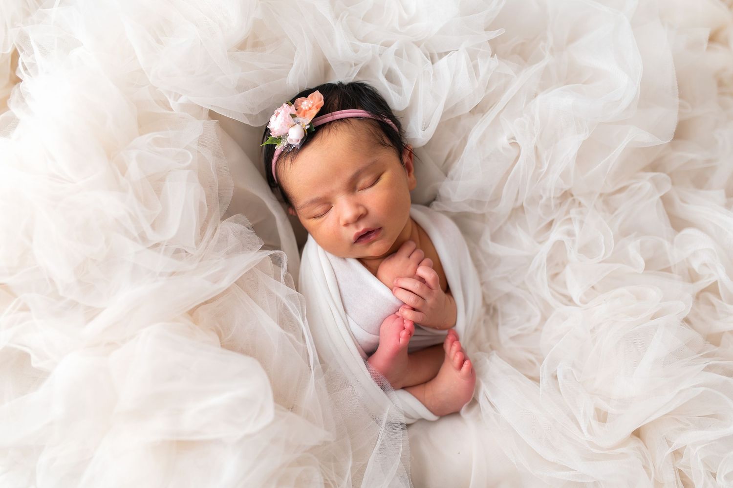 Peaceful newborn sleeping on white tulle fabric in dreamy portrait setting.