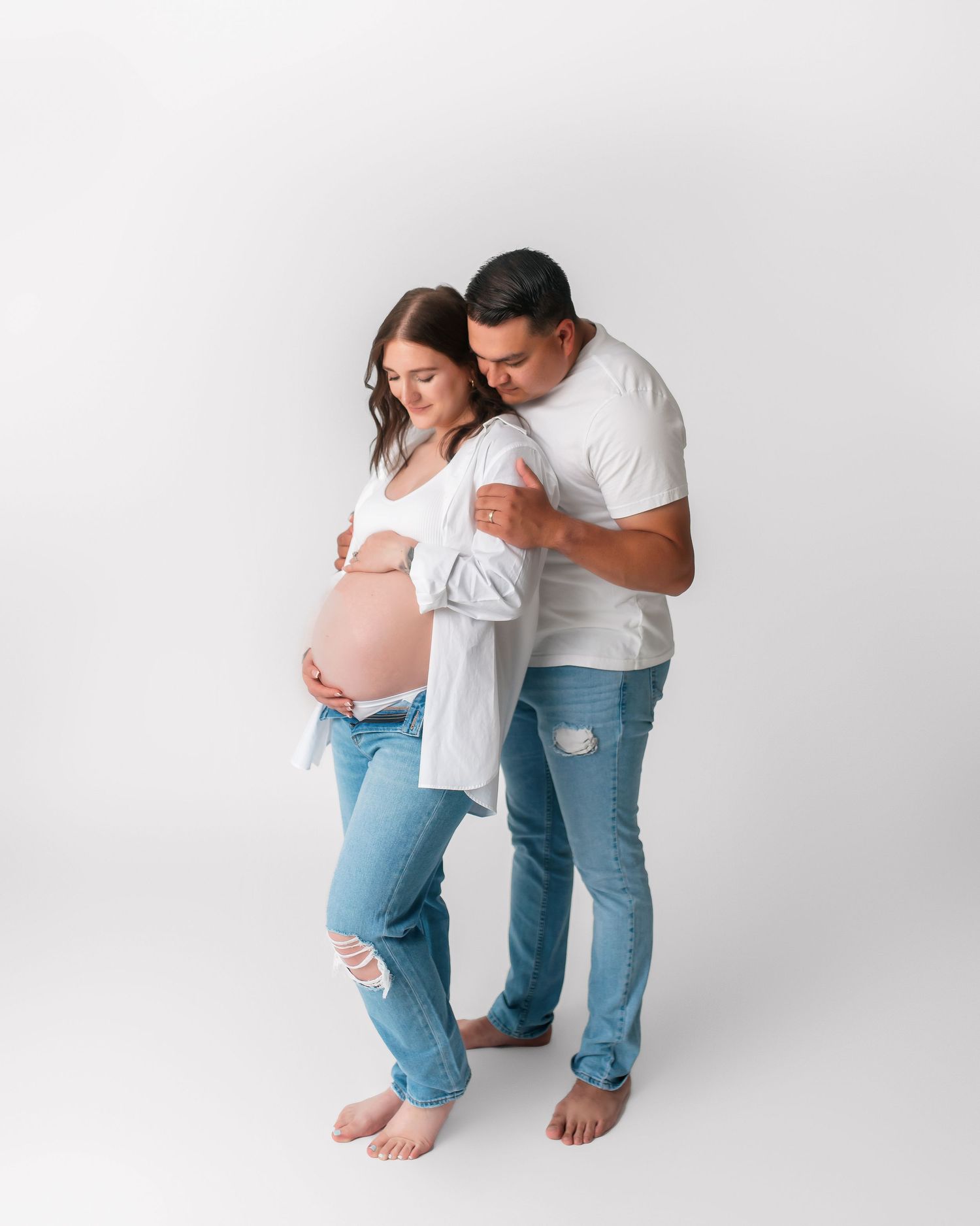 Sweet candid moment of couple during maternity photoshoot against white backdrop.