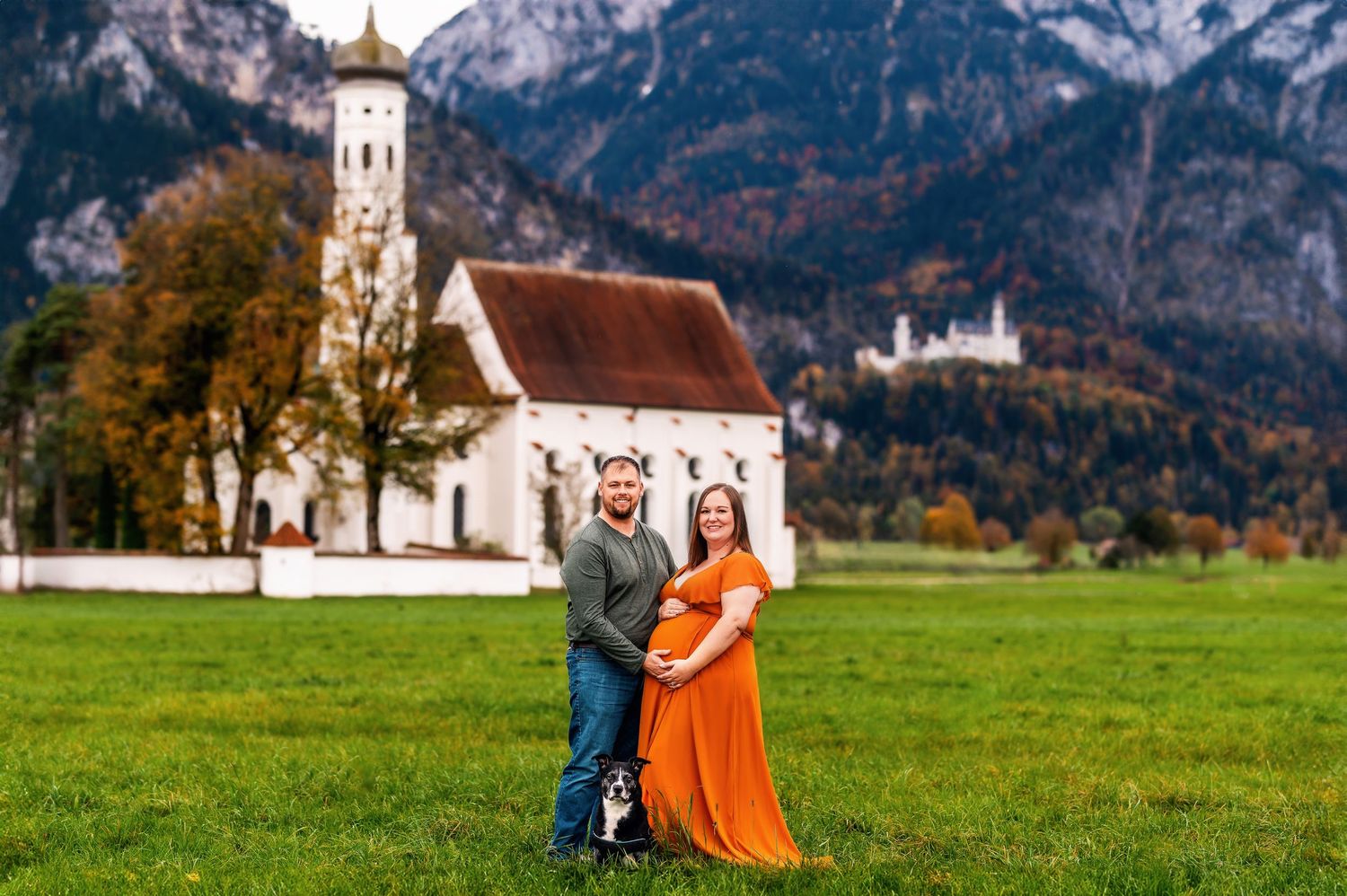 A couple poses in front of St. Coloman Church with the Bavarian Alps in the background near Schwangau, Germany.