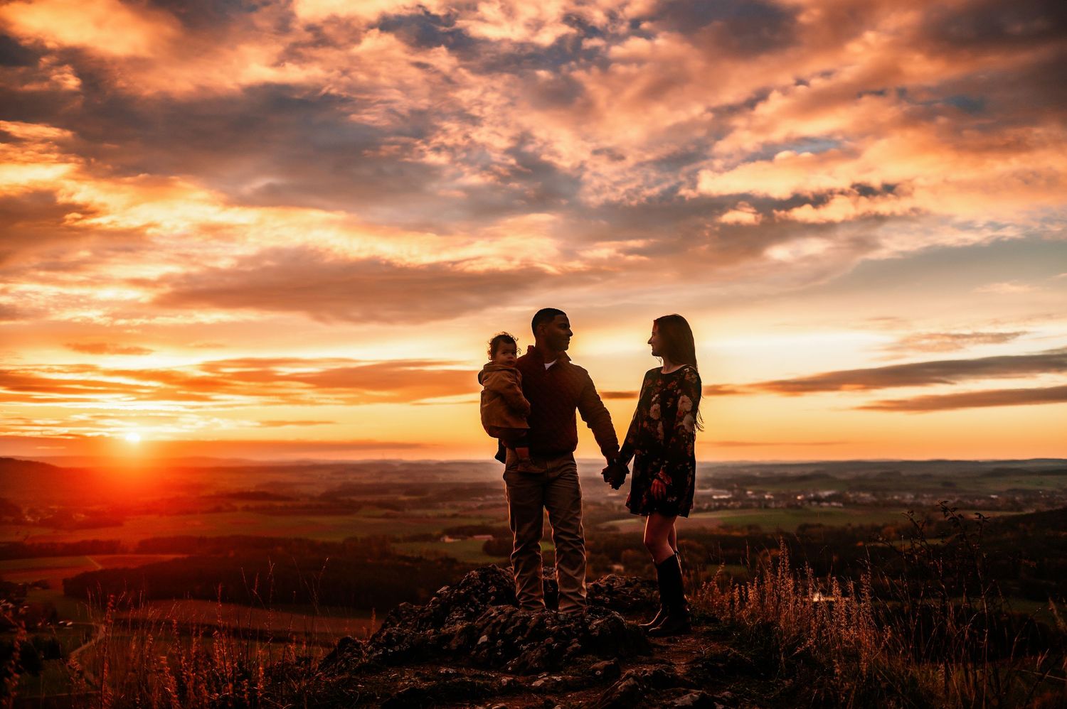 A family silhouetted against dramatic orange sunset sky on hilltop.