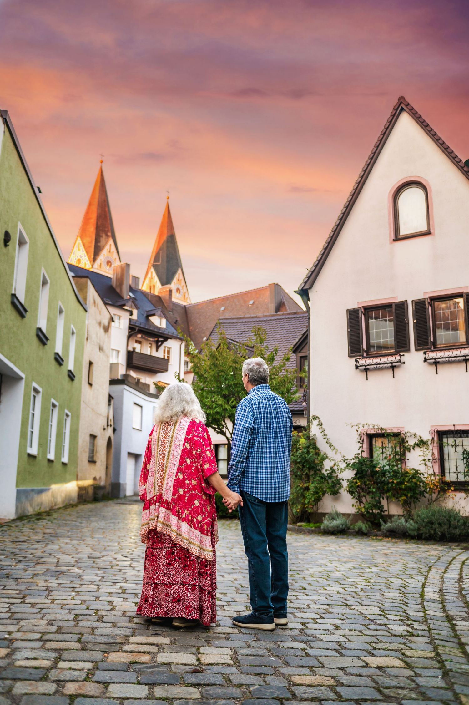 Couple admires historic European architecture and church spires at sunset on cobblestone street.