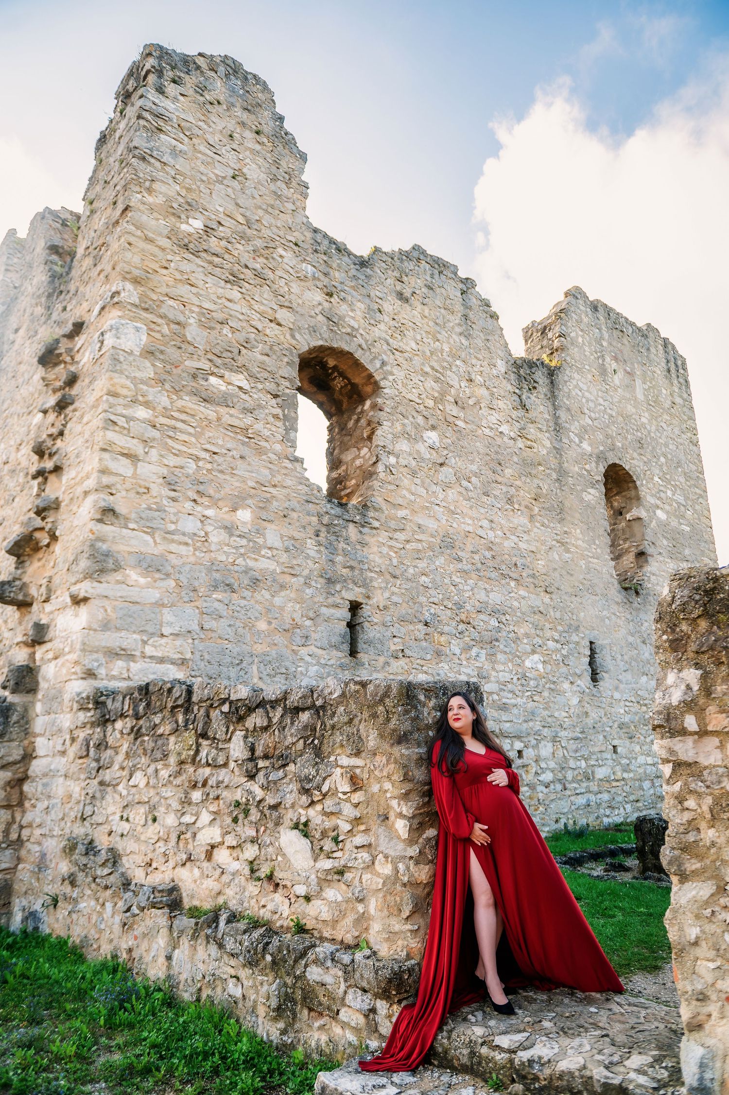 Ancient stone castle ruins with green grass and a flowing red cloak create a dramatic medieval atmosphere.