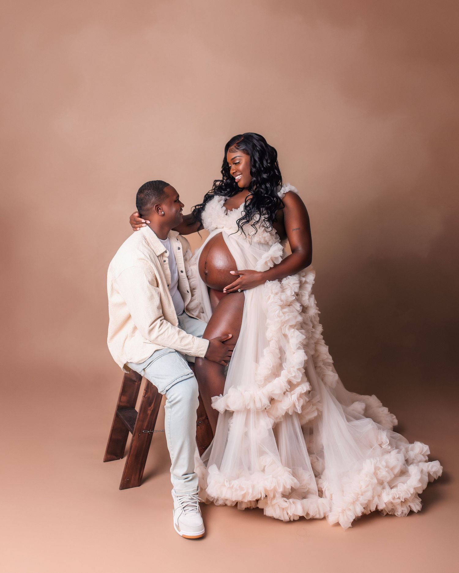 Romantic maternity shoot with expecting couple in light formal wear against warm backdrop.
