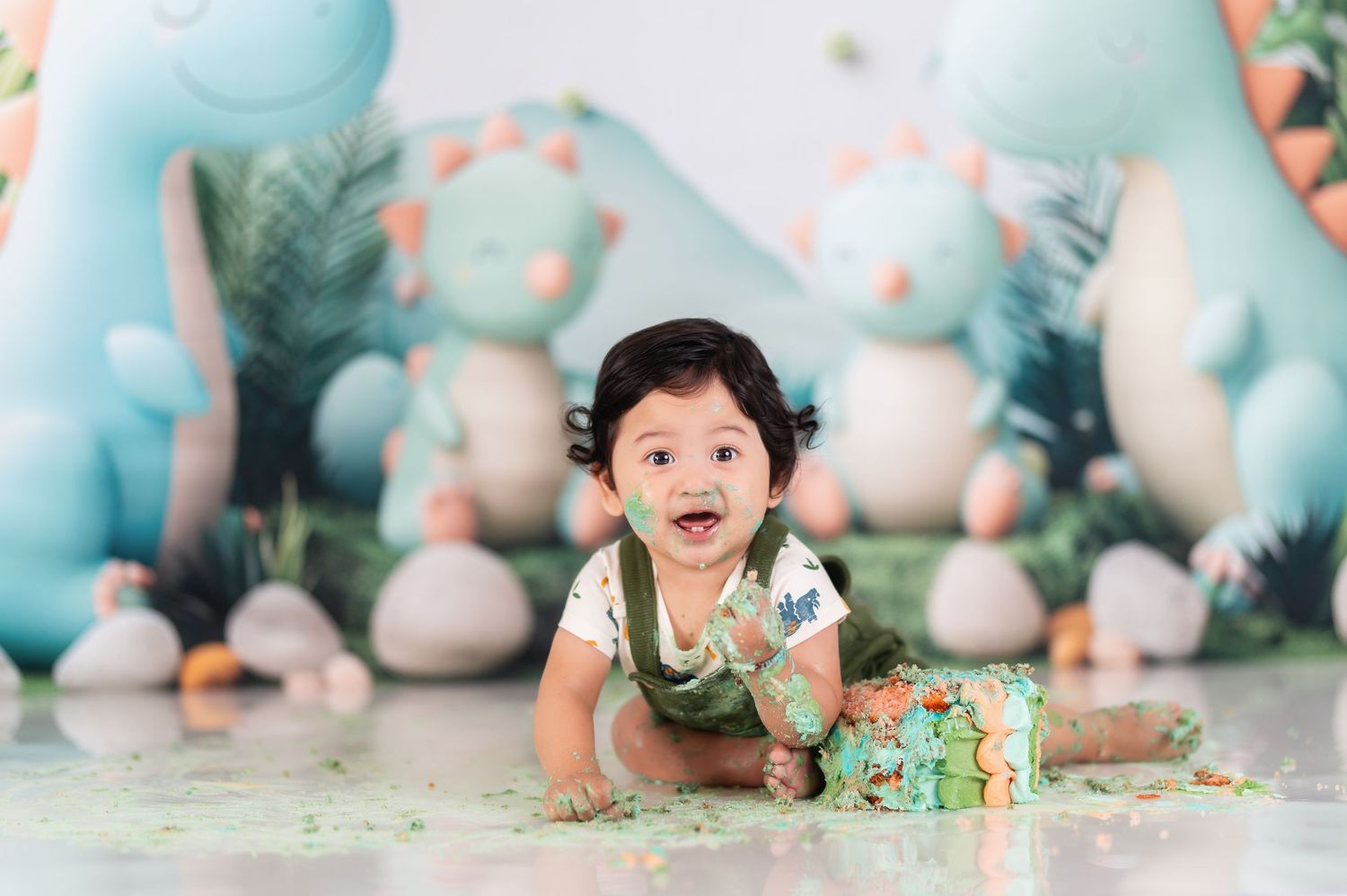 First birthday cake smash photo session with green dinosaur theme and balloon decorations.