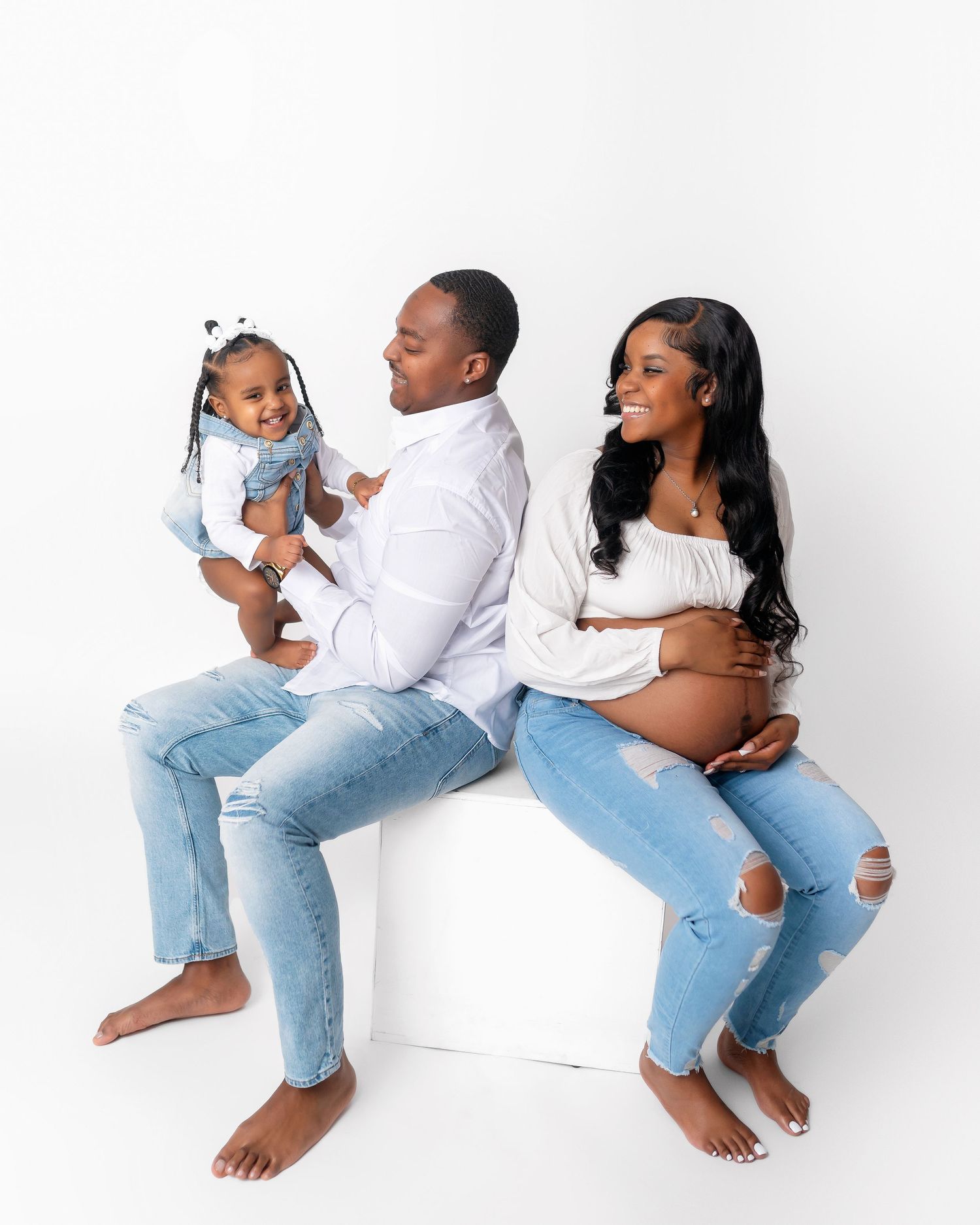 Modern family maternity photo featuring casual denim style against white background.