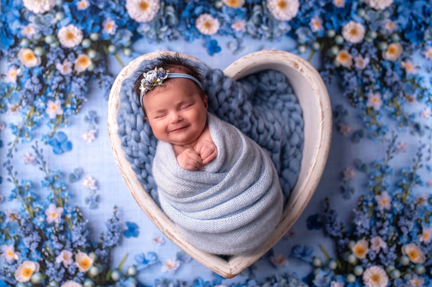 Newborn photography with baby wrapped in gray swaddle surrounded by blue and pink florals.