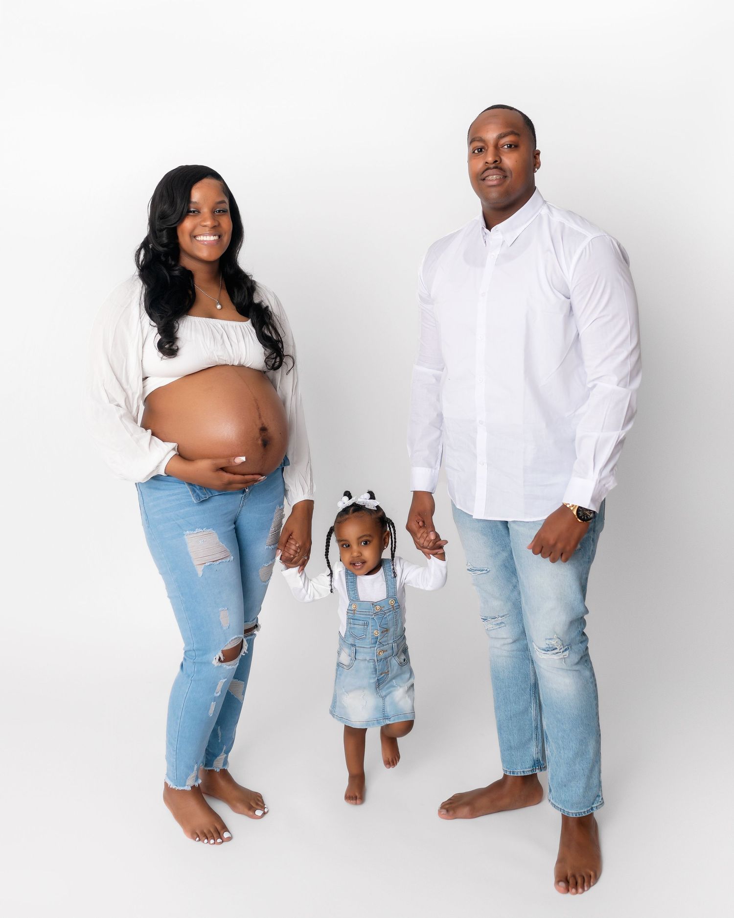 Casual family photo with expecting parents and toddler in matching denim and white.