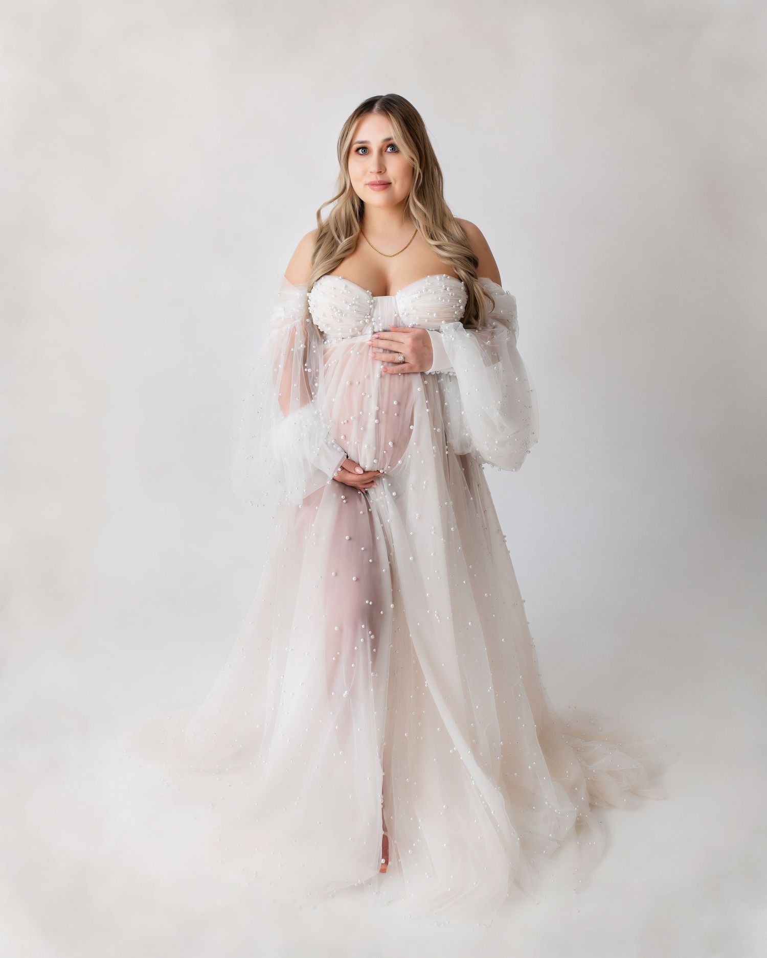 Ethereal maternity photo featuring a flowing white sheer gown with dramatic sleeves against a light backdrop.