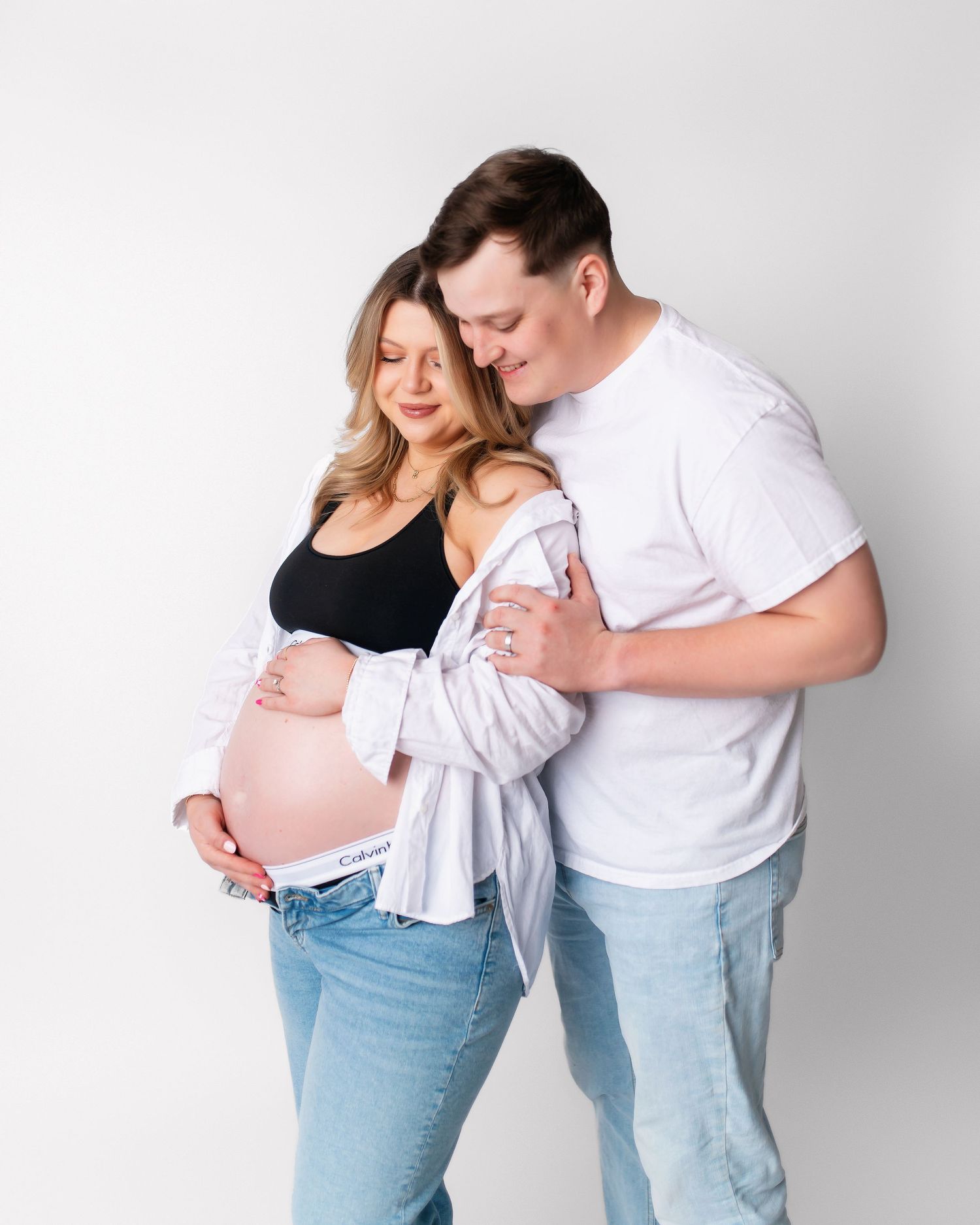 Couple shares intimate moment during maternity photoshoot wearing coordinated casual outfits.