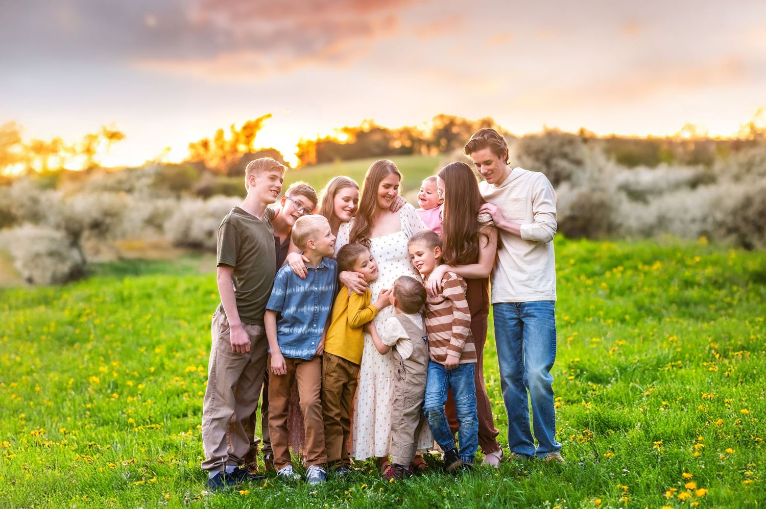 Large family group photo session in a grassy field during golden hour with casual coordinated outfits.