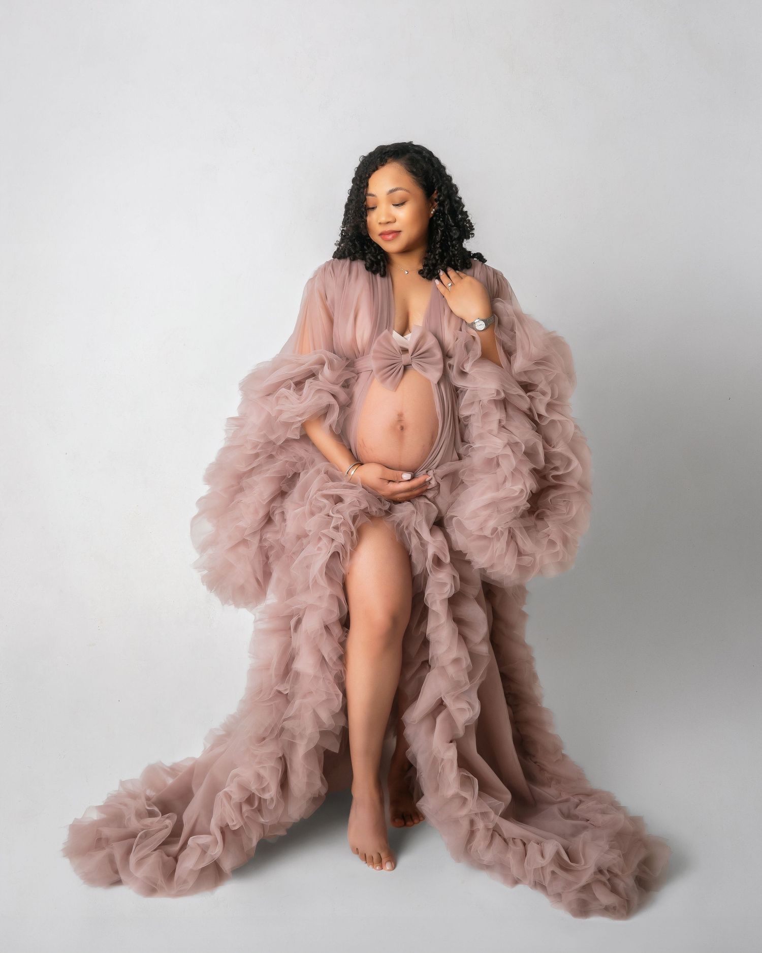 Maternity portrait in dusty rose ruffled gown against light background.