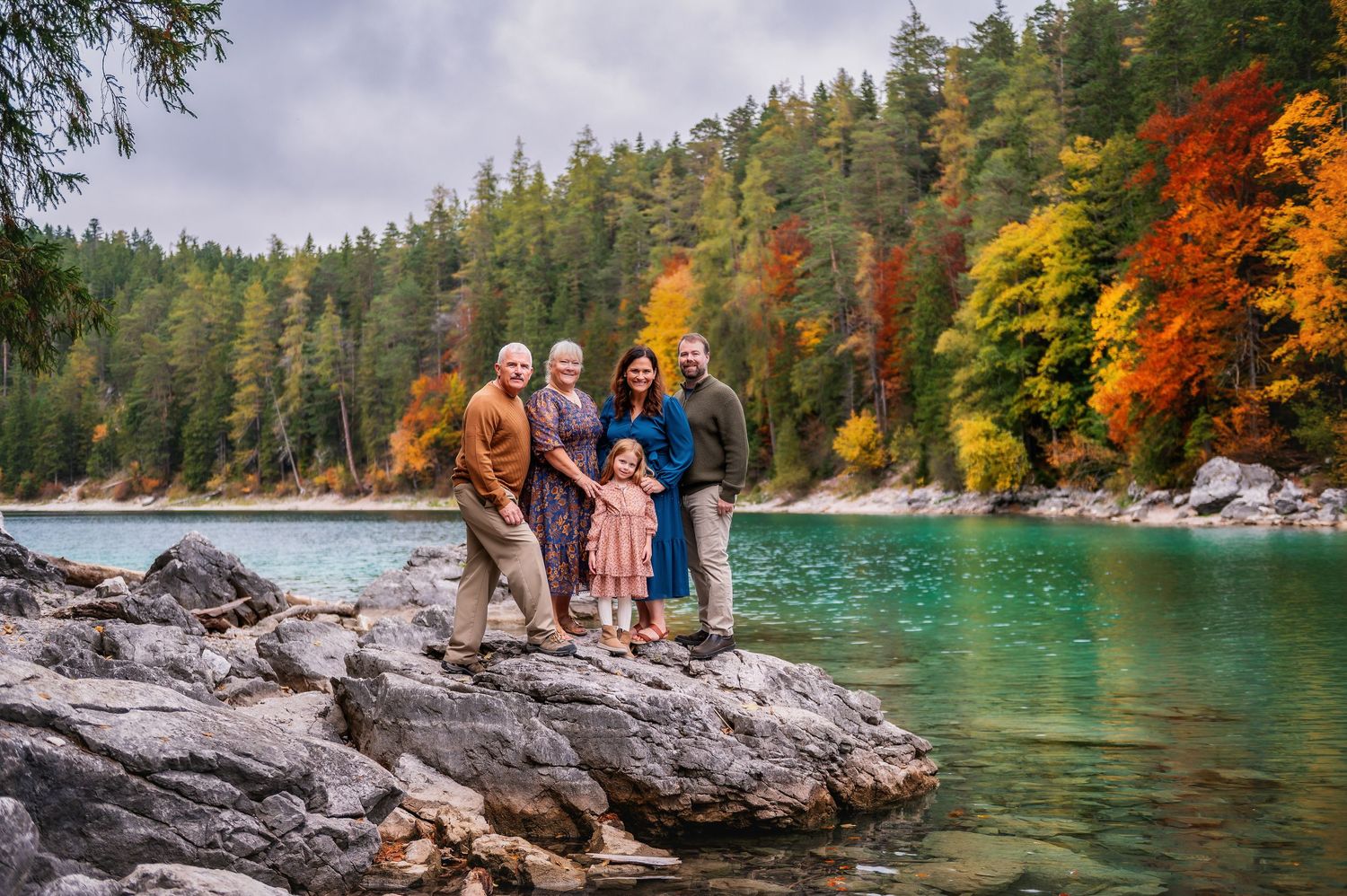 People enjoying the autumn scenery while sitting on rocky cliffs overlooking a turquoise lake surrounded by colorful trees.
