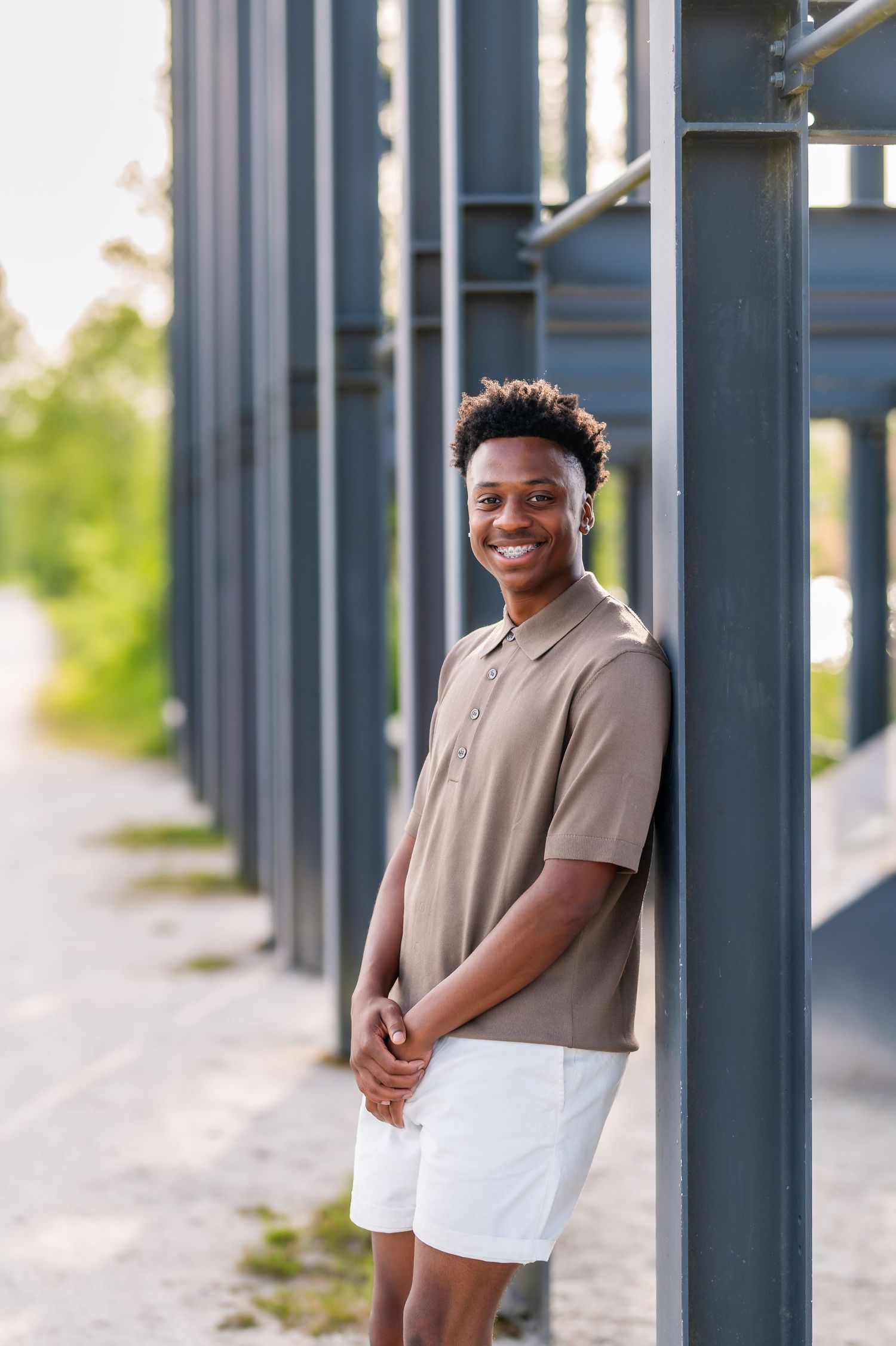 Person in beige polo and white shorts stands casually between modern architectural columns.