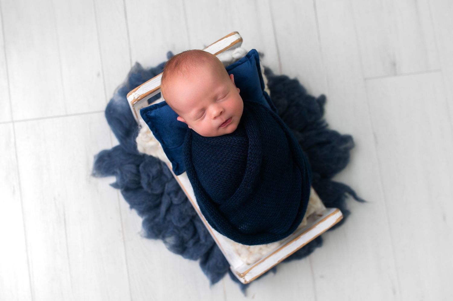 Peaceful sleeping newborn wrapped in navy blue blanket on white surface.