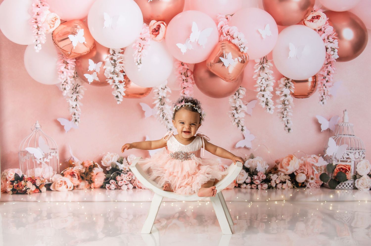 Pink balloon and floral backdrop for baby photography with white high chair setup.