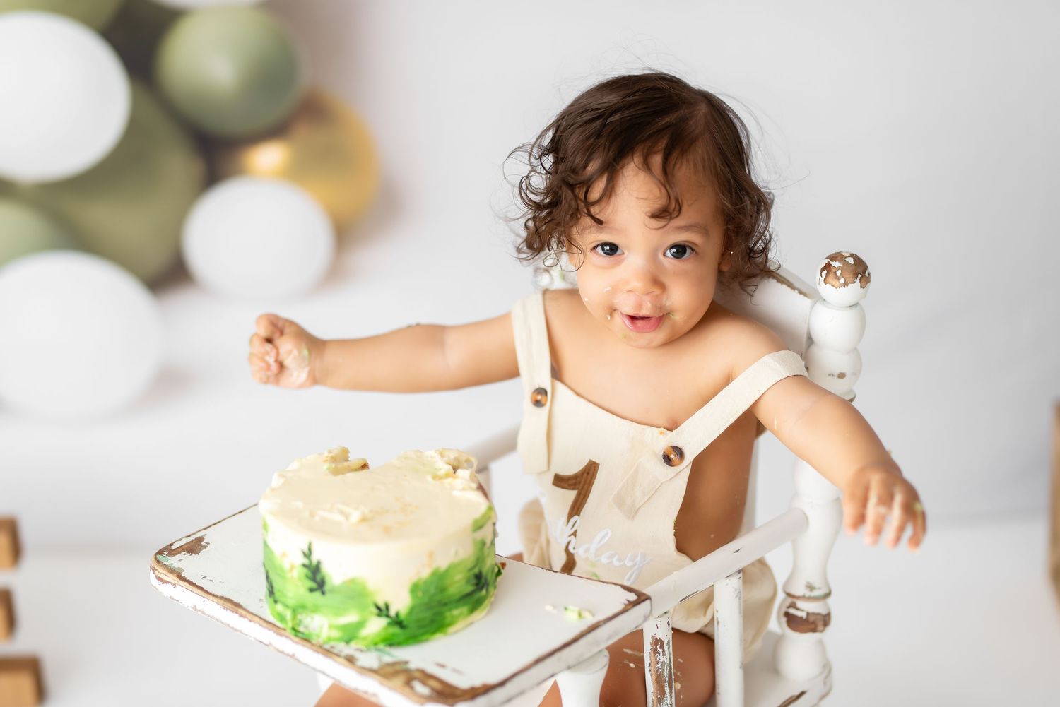 White high chair setup with green cake and balloon decorations for milestone photos.