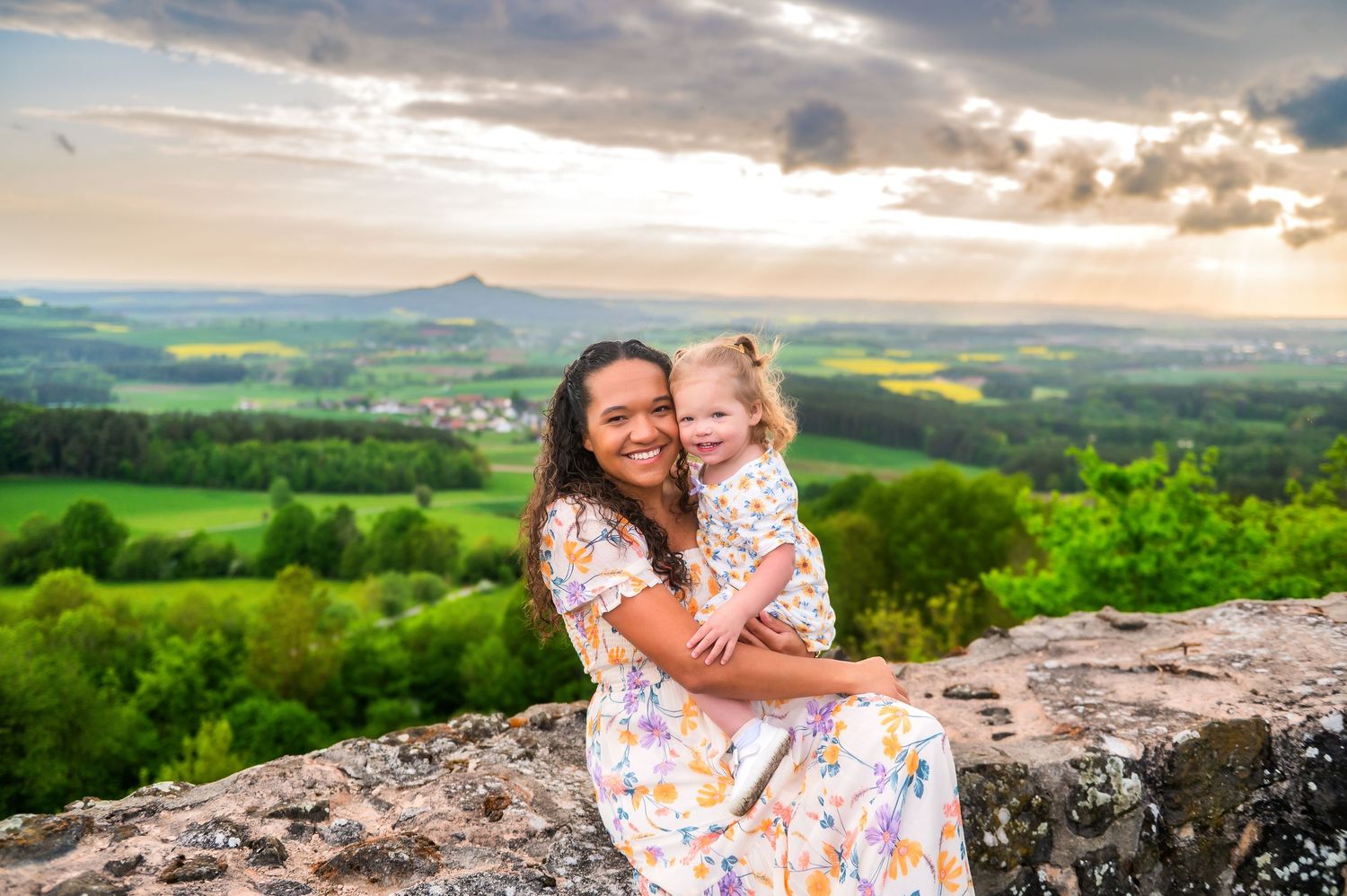 Family enjoying sunset views from a scenic overlook with stone wall and rolling hills in the background.