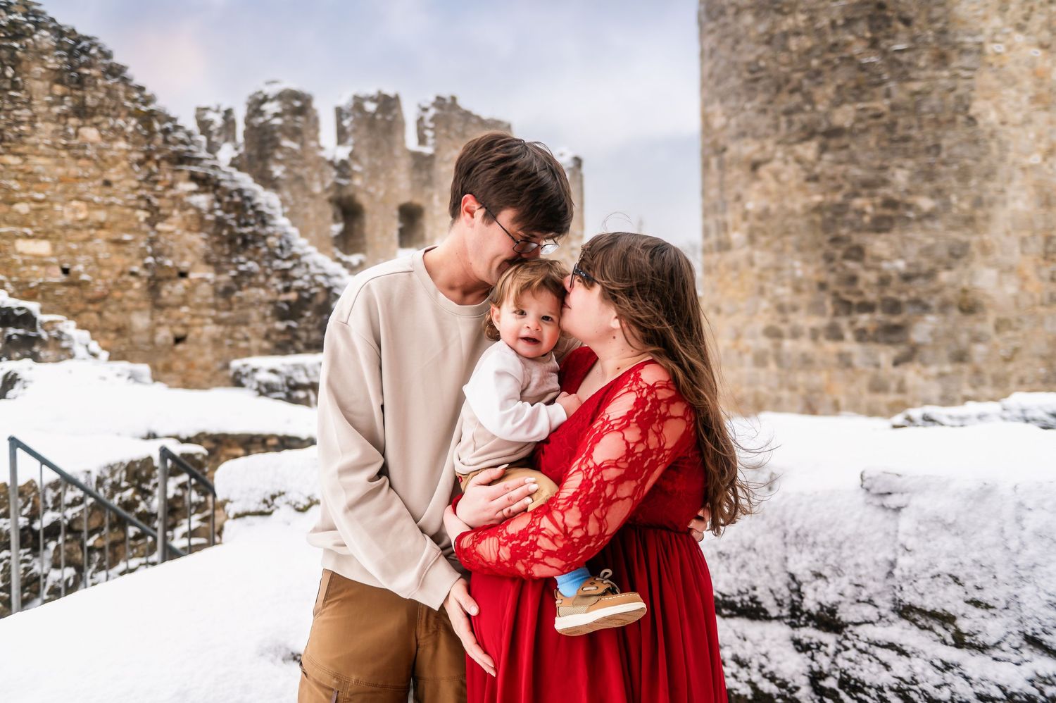Family sharing intimate moment by snow-covered castle ruins in winter setting.