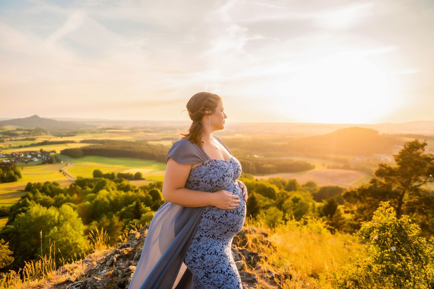 A peaceful maternity photo showcases a pregnant woman overlooking rolling hills at golden hour.