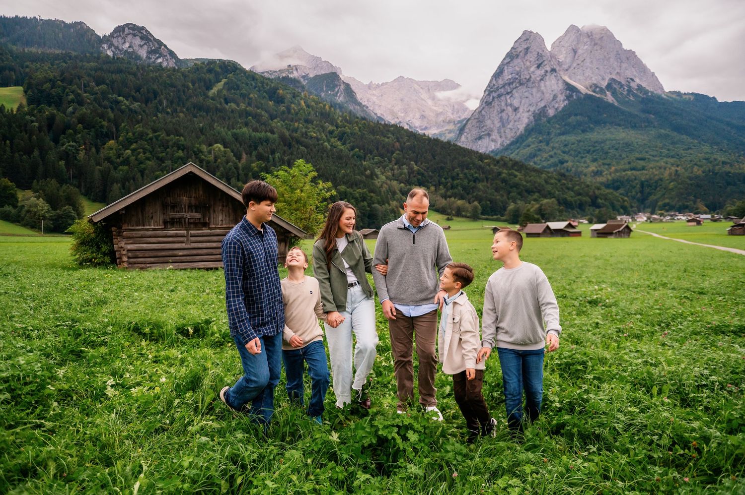 A group of people walking together through a lush green meadow with majestic mountain peaks in the background.