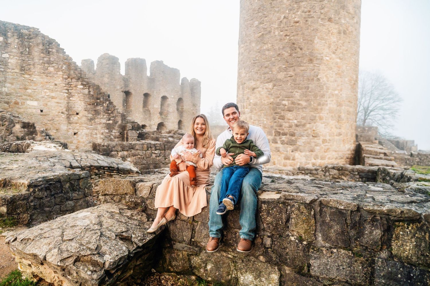 Couple sitting on ancient stone ruins of a castle wall with architectural details in background.
