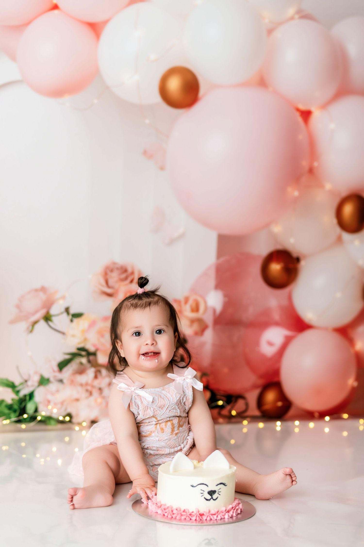 Pink and rose gold balloon arch with floral details for cake smash photography.