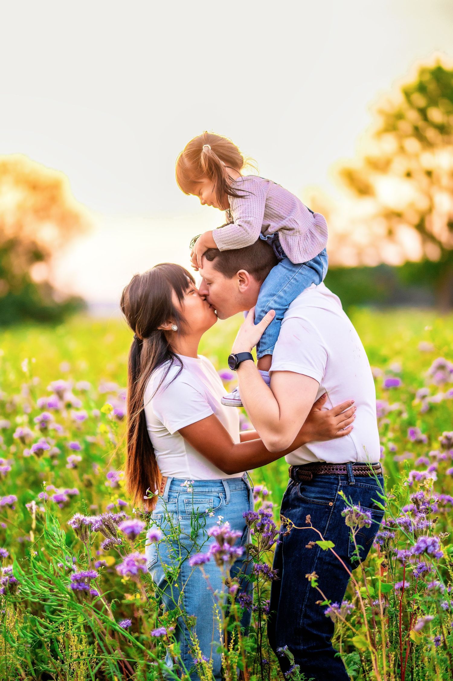 Family of three shares tender moment in blooming wildflower meadow at sunset.