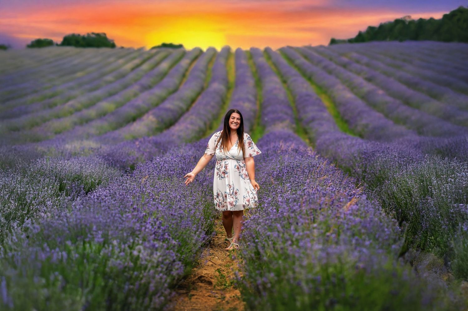A figure in a floral dress walks through rows of purple lavender fields during a vibrant sunset in Provence, France.