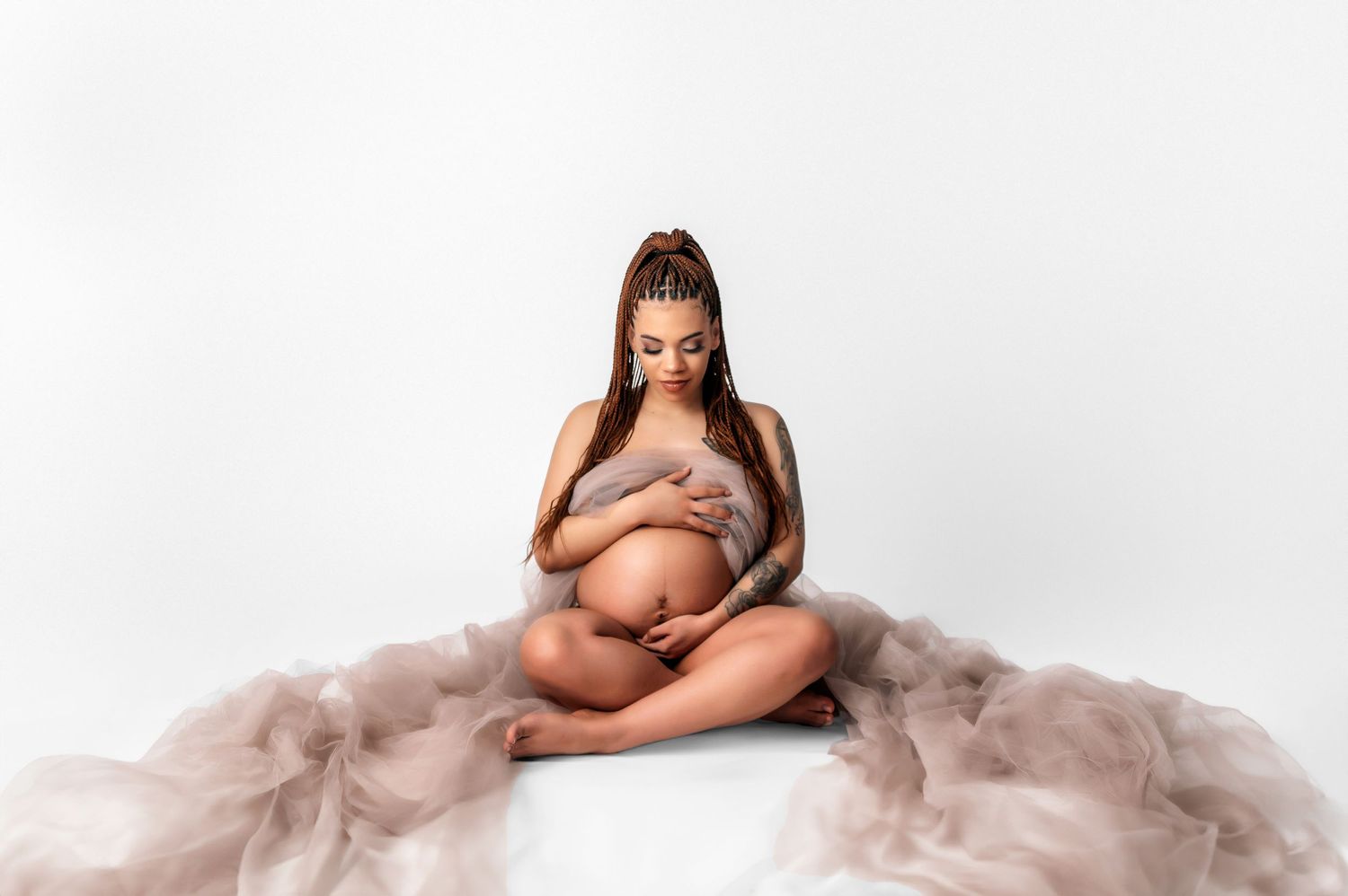 Intimate maternity portrait with soft pink tulle fabric on white background.