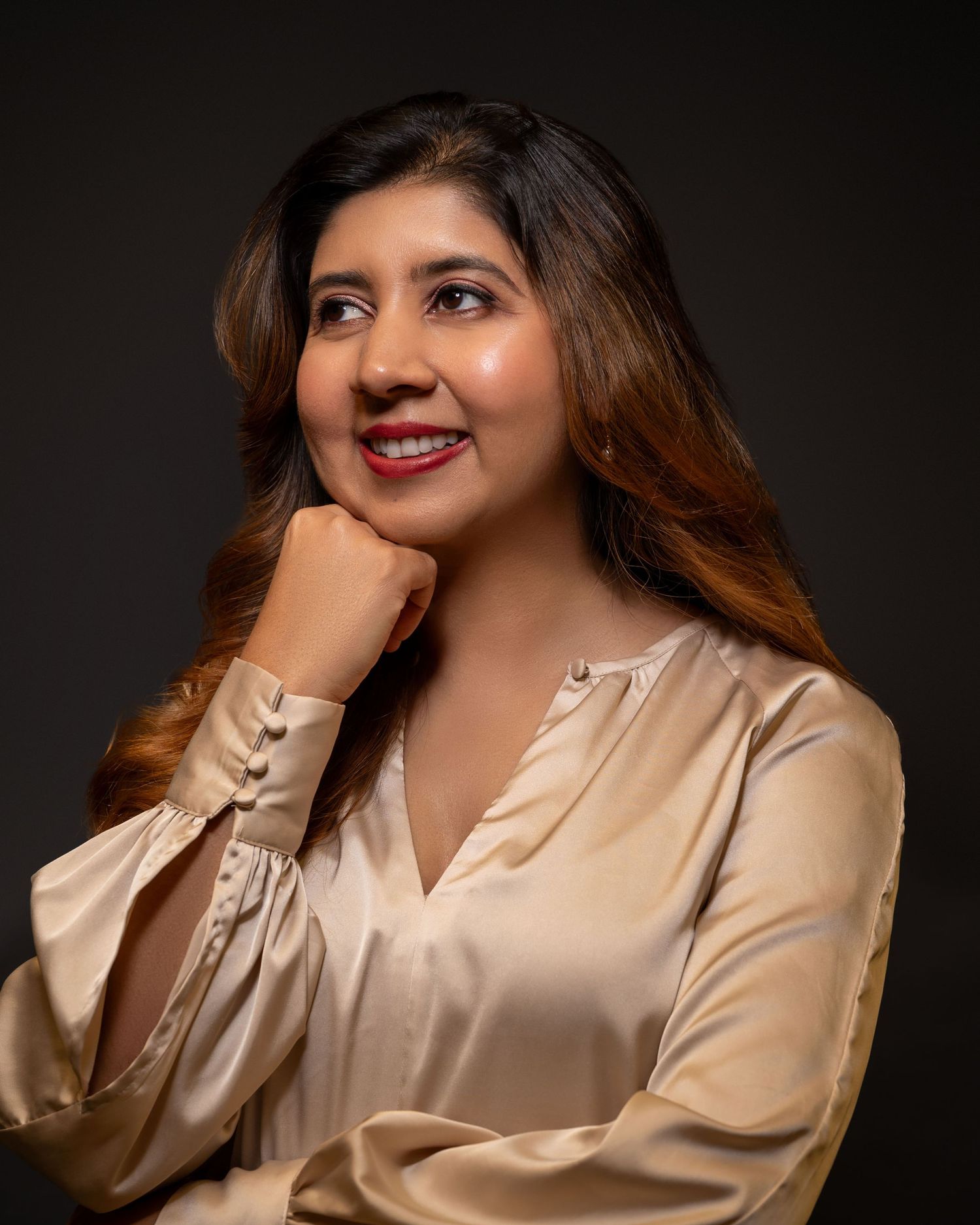 Woman in beige silk blouse poses elegantly against dark background in studio portraits.