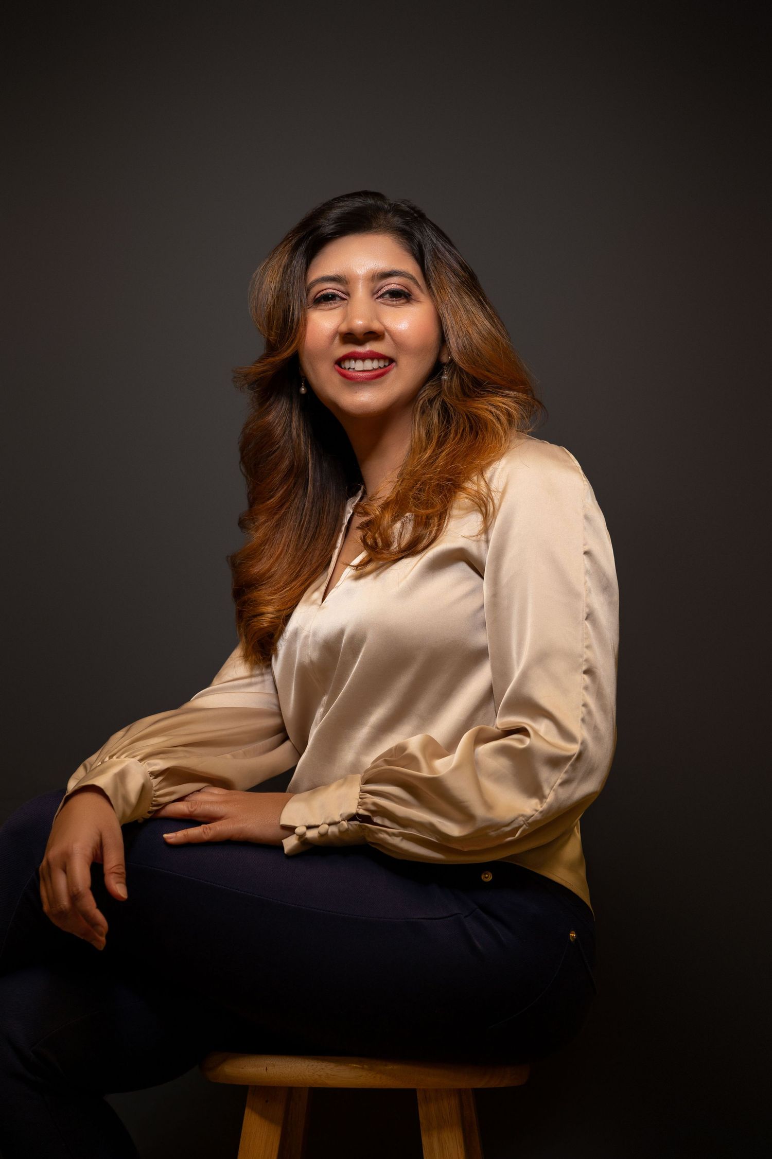 Studio portrait with soft lighting showing a beige silk blouse against dark background.