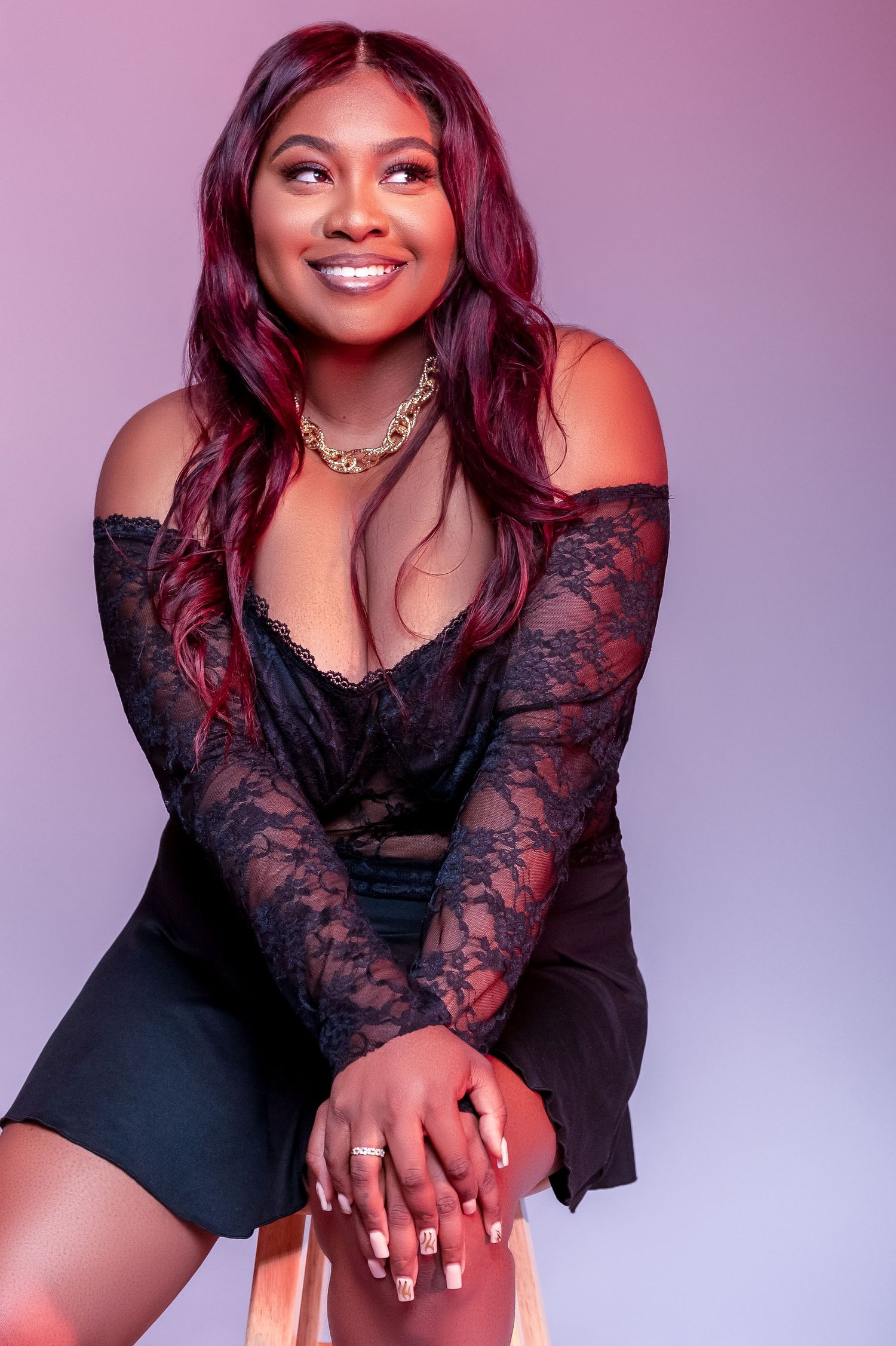 Woman in black lace dress poses against purple backdrop for professional photoshoot.