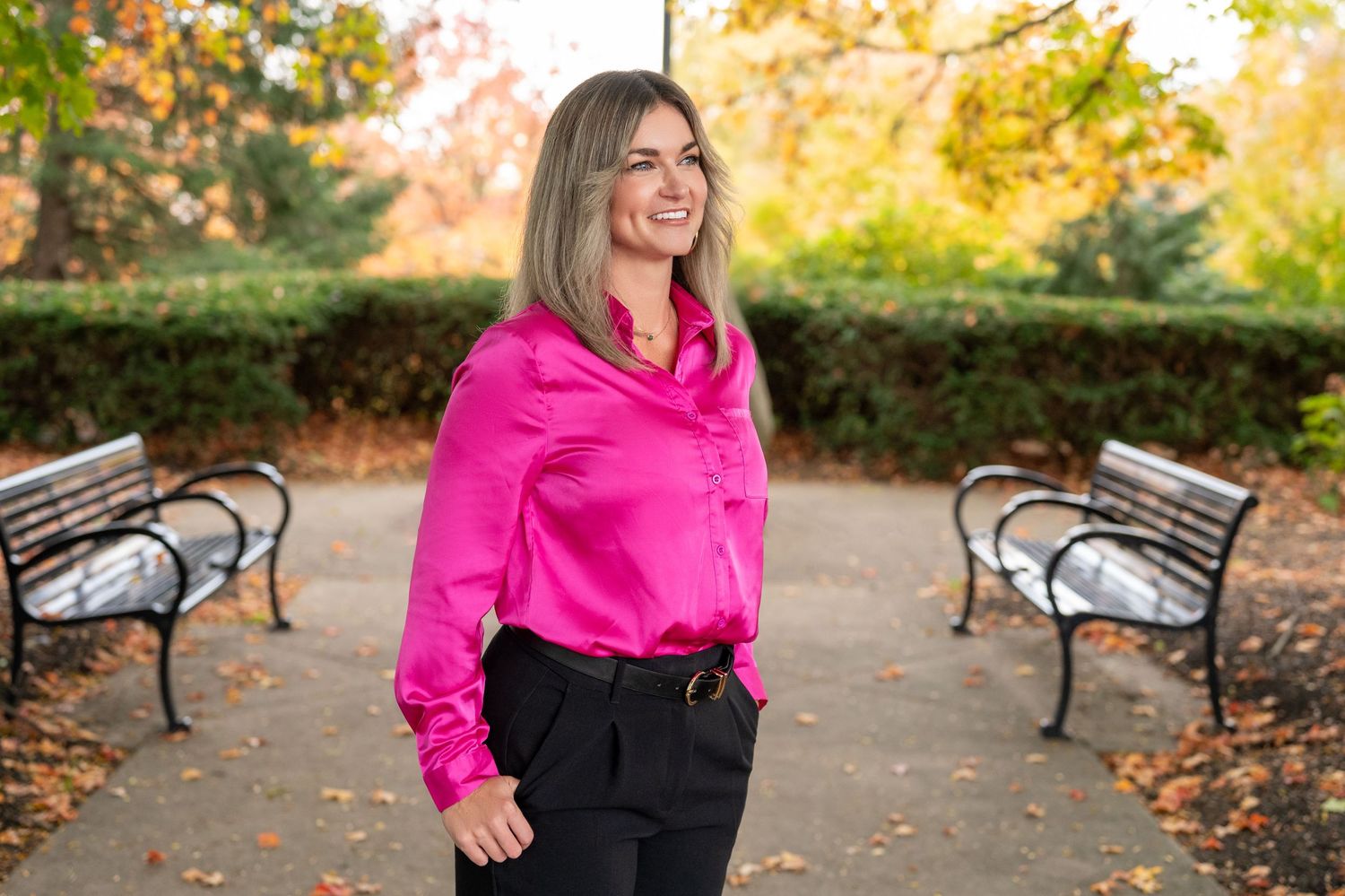 Professional outdoor portrait in a park setting featuring bright pink blouse and black pants on an autumn day.