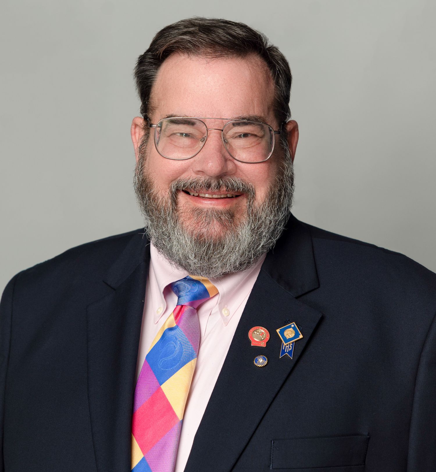 Professional headshot of a person wearing glasses and a colorful striped tie with a navy suit jacket.