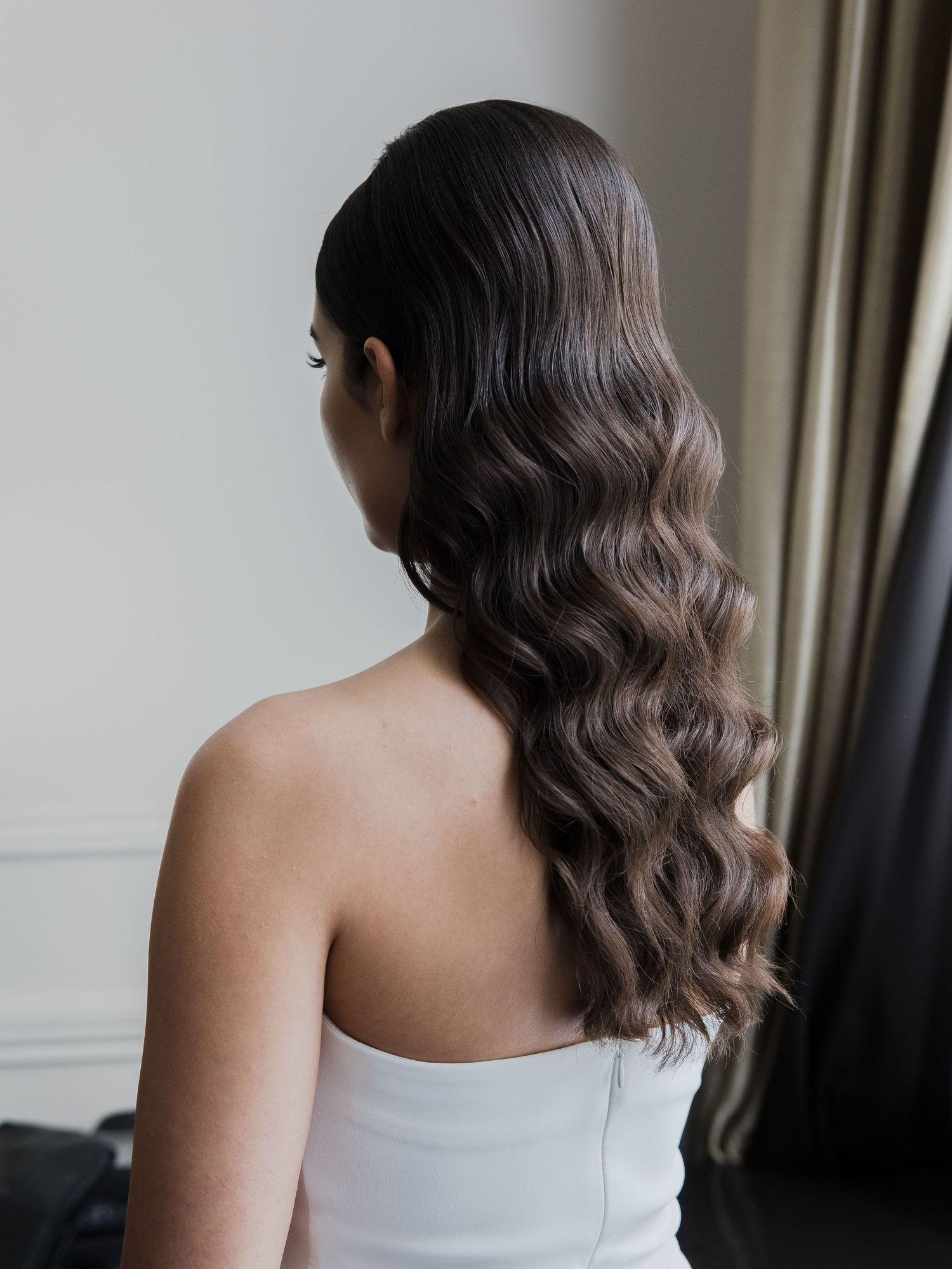 Back view of white formal dress with elegant wavy hairstyle.
