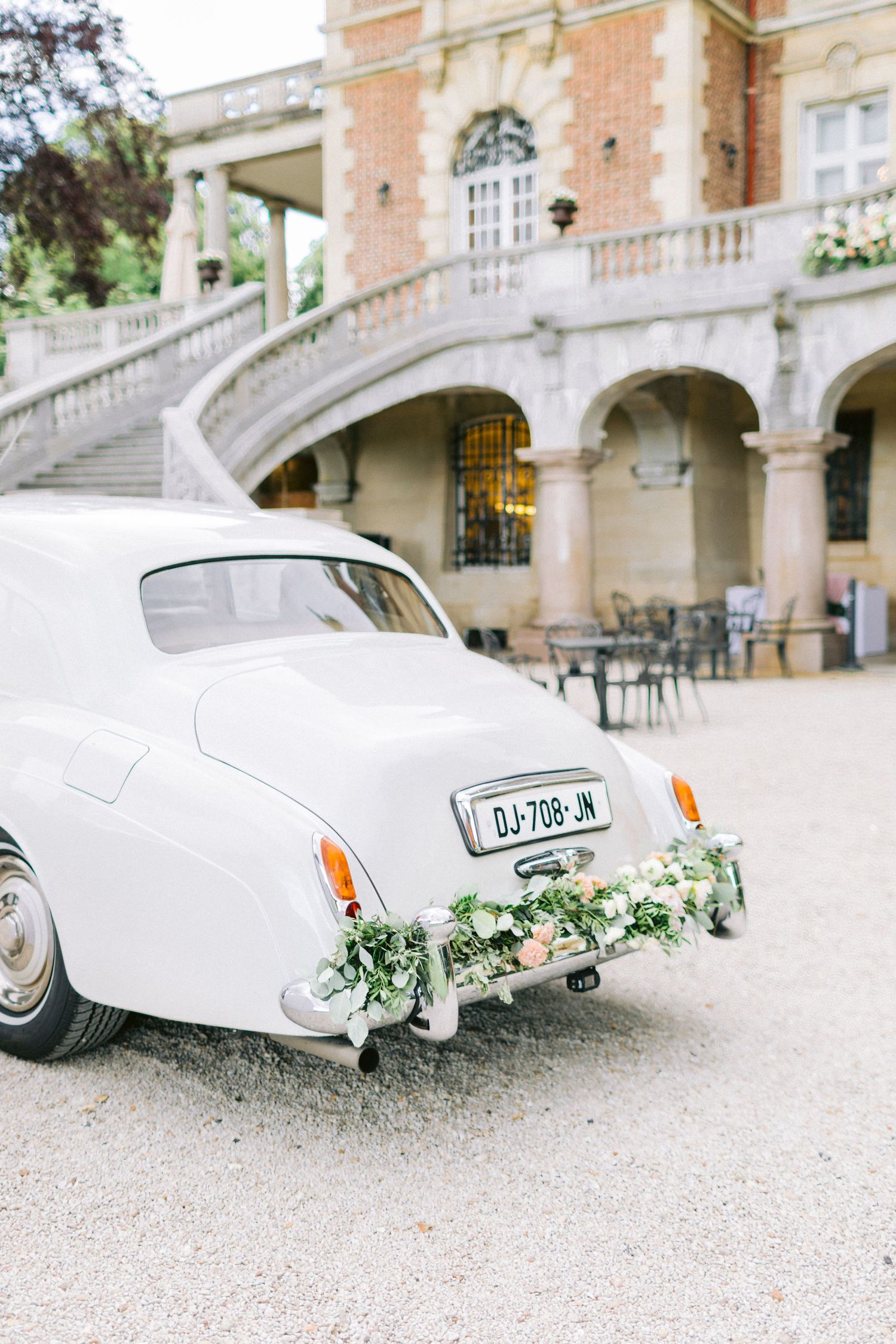 Classic white vintage car decorated with flowers parked outside an elegant stone building.